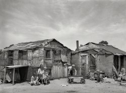 July 1939. "Family in front of shack home. May Avenue camp, Oklahoma City." Photo by Russell Lee for the Farm Security Administration. View full size.