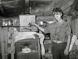 July 1939. "Boy living in camp near May Avenue, Oklahoma City. Photographs show exterior and interior of shacks, tents, other makeshift shelter in May Avenue camp which is partially under bridge and adjacent to city dump and hog wallow. Squalor, filth, vermin in which poverty-stricken inhabitants dwell. Water supplied by shallow wells and water peddler. Piles of rubbish and debris in which children and adults have injured feet. Privies. Families eating food from vegetable dumps, packing houses and discarded from hospital. Children clothed in gunny sacks. Malnourished babies. Sick people. Cooking, washing, ironing, patching. Improvised chicken coop. Corn patch." Acetate negative by Russell Lee. View full size.