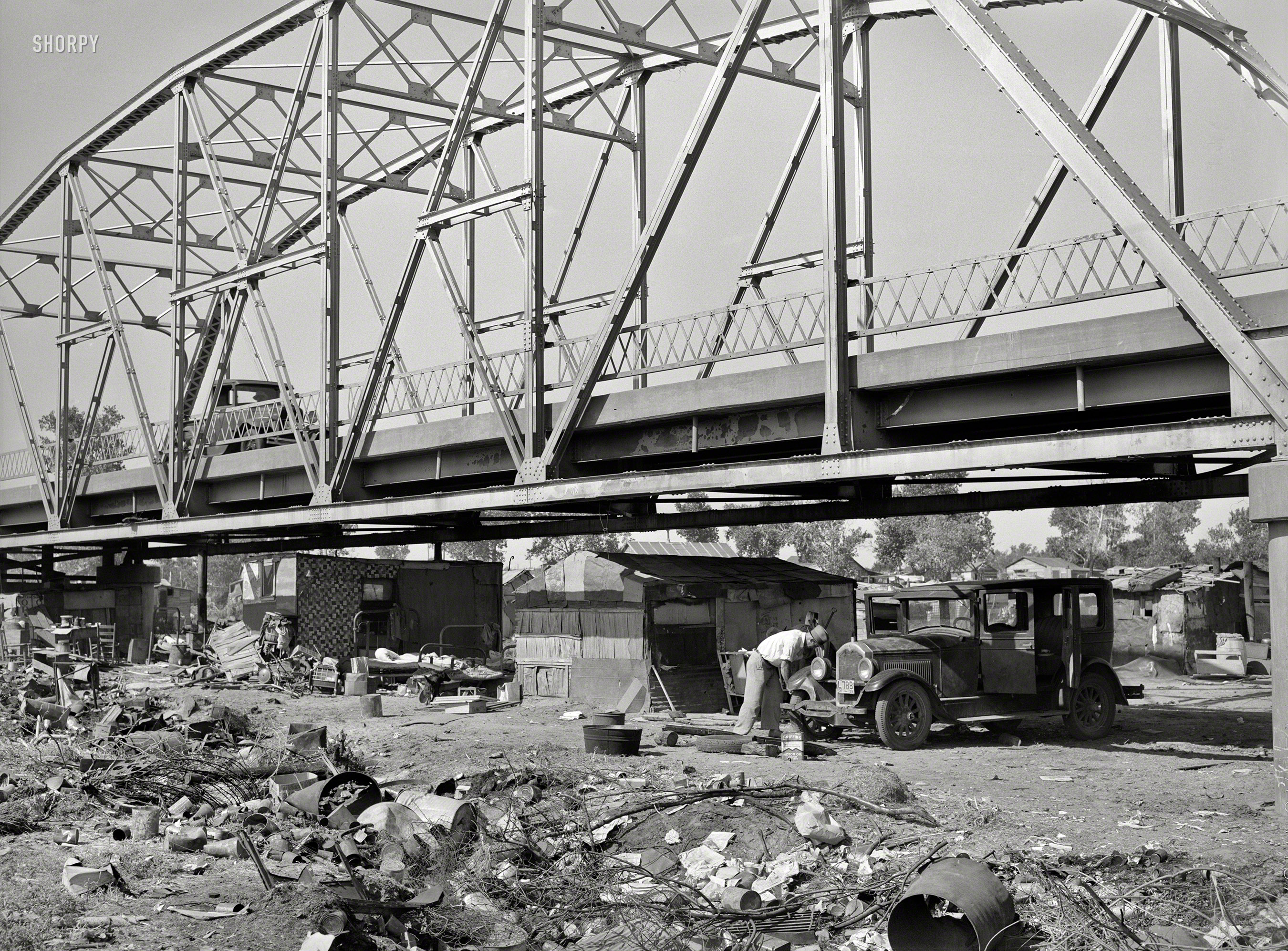 July 1939. Oklahoma City. "Shacks, tents, other makeshift shelter in May Avenue camp, which is partially under bridge and adjacent to city dump and hog wallow. Photographs show squalor, filth and vermin in which poverty-stricken inhabitants dwell. Water supplied by shallow wells and water peddler. Piles of rubbish and debris in which children and adults have injured feet. Privies. Families eating food from vegetable dumps, packinghouses and discarded from hospital. Children clothed in gunny sacks. Malnourished babies. Sick people. Cooking, washing, ironing, patching. Improvised chicken coop. Corn patch." Medium format negative by Russell Lee for the Farm Security Administration. View full size.