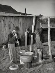February 1940. "Sons of Pomp Hall, Negro tenant farmer, drawing water and mixing bran mash to feed the hogs. Creek County, Oklahoma." Medium format negative by Russell Lee for the Farm Security Administration. View full size.