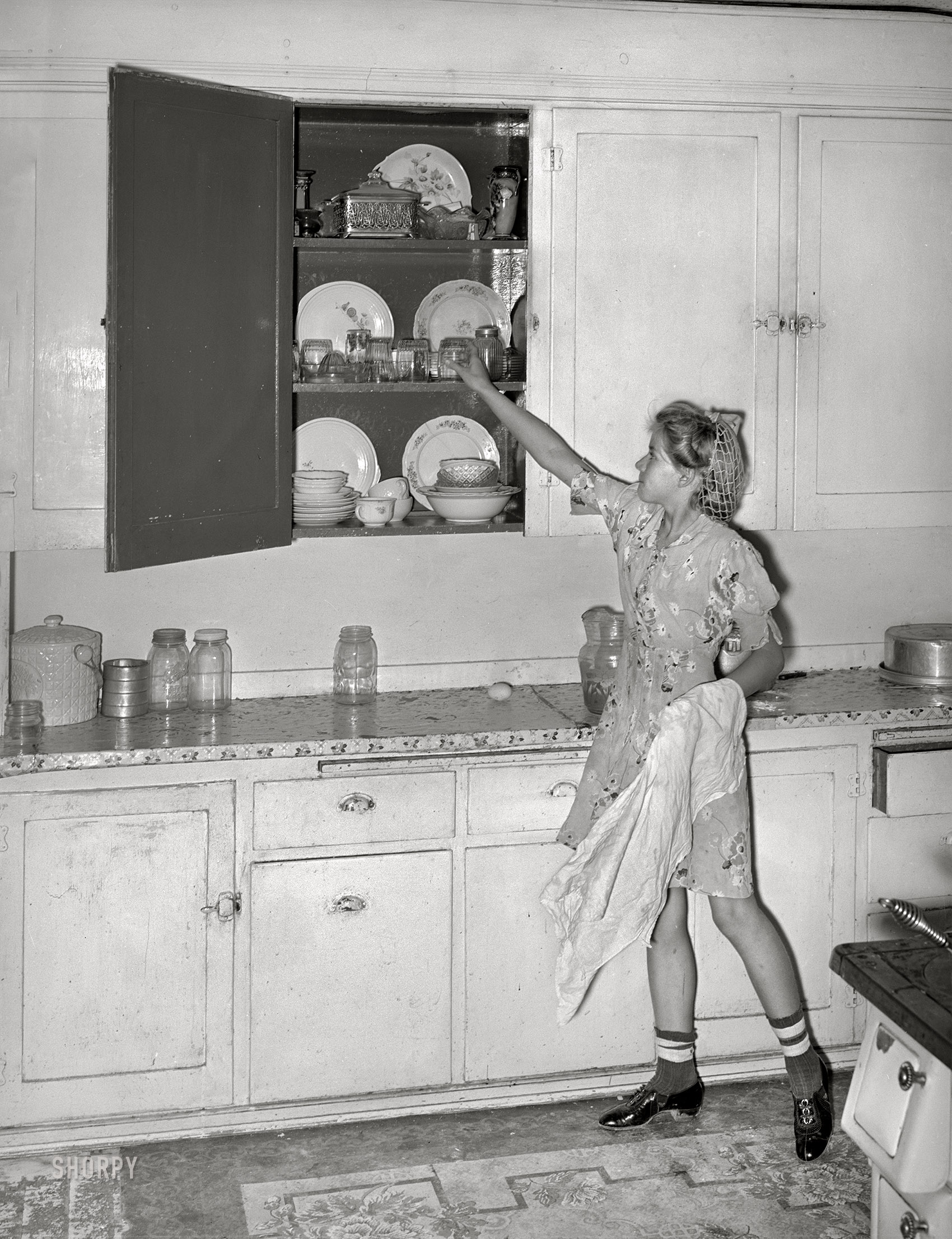 August 1940. "Daughter of Mormon farmer putting away dishes in kitchen cabinet. Box Elder County, Utah." Photo by Russell Lee for the Farm Security Administration. View full size.