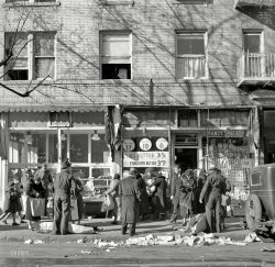 December 1936. "Scene along Bathgate Avenue in the Bronx, a section from which many of the New Jersey homesteaders have come." Photo by Arthur Rothstein for the Resettlement Administration, which used these pictures as examples of the supposed squalor from which it was rescuing its clients -- second-generation Jewish immigrant families -- by relocating them to the suburbs. View full size.
Rosenbaum&#039;s Dairywas located at 1619 Bathgate Avenue, Bronx NY according to the 1940 NY Telephone Directory. JErome 7-7139. All gone now.
Staged SceneLooks like a staged street scene judging from the very nice clothing being worn by the people.
[That's normal garb for the period and circumstances. -tterrace]
Not too shabbyI would agree that the street was very messy and unkempt but all of the people are neatly and warmly dressed and do not appear to be living in squalor.  Everyone has warm coats, hats and shoes, including the two school girls carrying their books through the crowd.  People are even paying attention to the vendors selling their wares from sheets on the streets (they used pushcarts on the lower east side, even into the 1950's and 60's).  By employing a street cleaner, this scene could be much tidier. 
Squalor?Somebody grab a broom - problem solved.  Careful, don't sweep up that logo.
Expensive Butter?Both of my inflation calculators say that $.27 in 1936 translates to $6.30 today.  That means it was fairly expensive at the bottom of the Great Depression.
Billy BathgateThe hero of Billy Bathgate (1989) by E.L. Doctorow, set in the year before this photo was taken, is named for Bathgate Avenue in the Bronx.  In one section of the novel, the teen narrator differentiates between the street vendors, with their pushcarts and open stalls, and the "aristocracy of the business" who had "real stores where you walked in and bought your chickens still in their feathers, or your fresh fish, or your flank steak, or milk and butter and cheese, or lox and smoked whitefish and pickles."
(The Gallery, NYC, Stores & Markets)