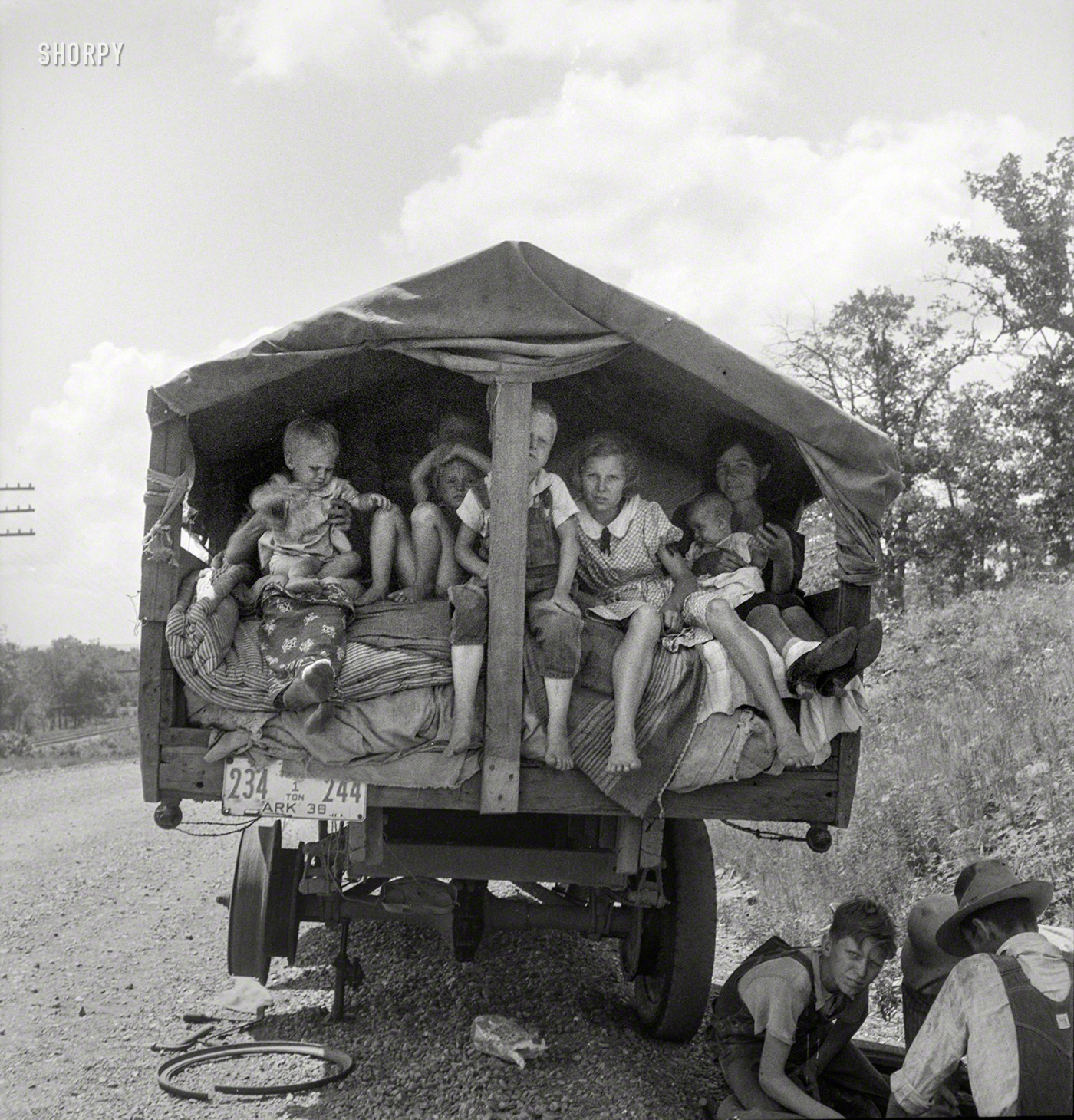 June 1938. "On highway No. 1 of the 'OK' state near Webbers Falls, Muskogee County, Oklahoma. Seven children and eldest son's family. Father was a blacksmith in Paris, Arkansas. Son was a tenant farmer. 'We're bound for Kingfisher (Oklahoma wheat) and Lubbock (Texas cotton). We're not trying to but we'll be in California yet. We're not going back to Arkansas; believe I can better myself'." Photo by Dorothea Lange for the Resettlement Admin. View full size.