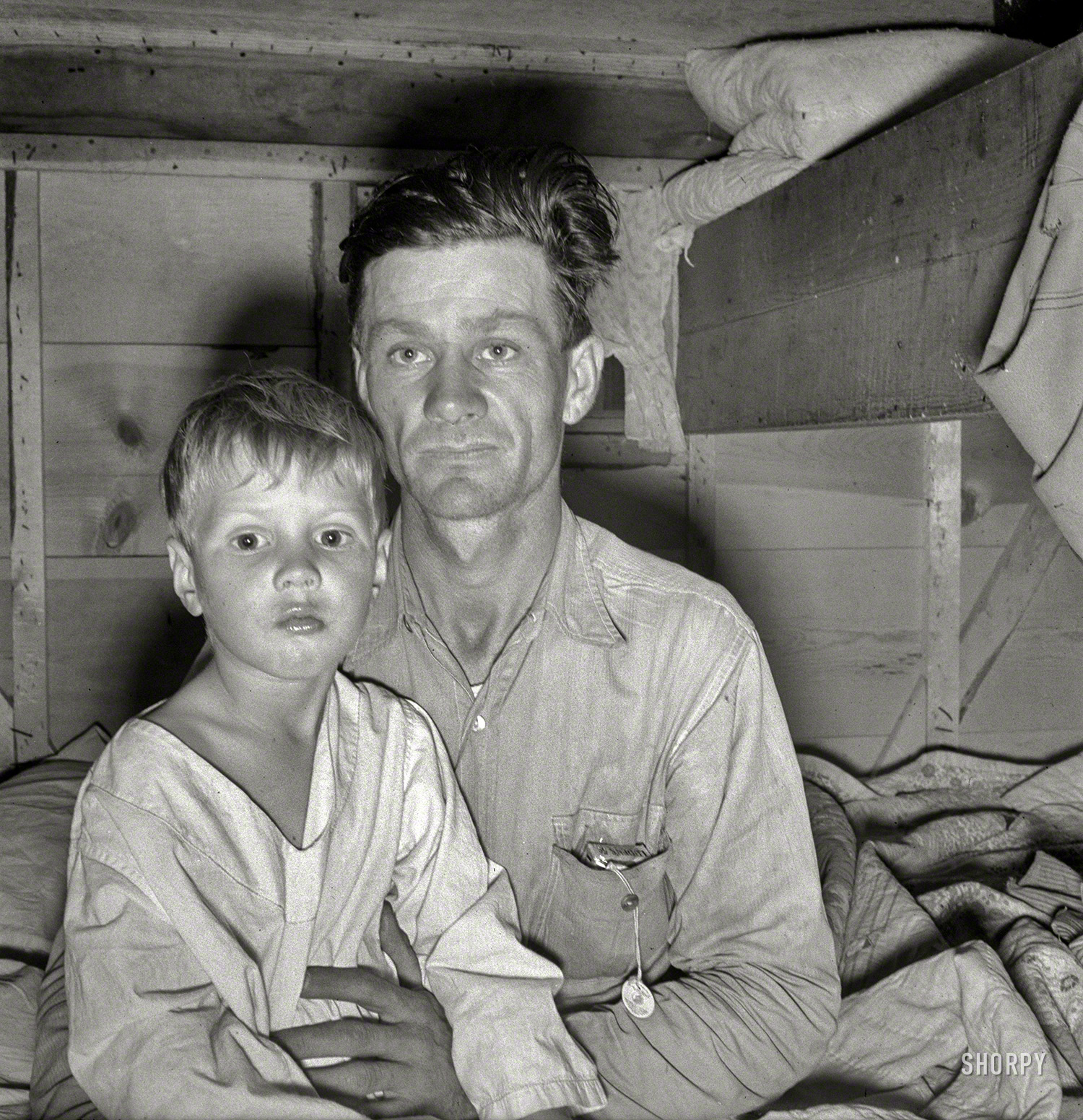 October 1939. "He brought his family to the West in a homemade trailer from Texas five months ago. Photograph made after supper. Boy sick. Father has work now in potato field. Merrill, Klamath County, Oregon. In mobile unit, FSA camp." Photo by Dorothea Lange for the Farm Security Administration. View full size.