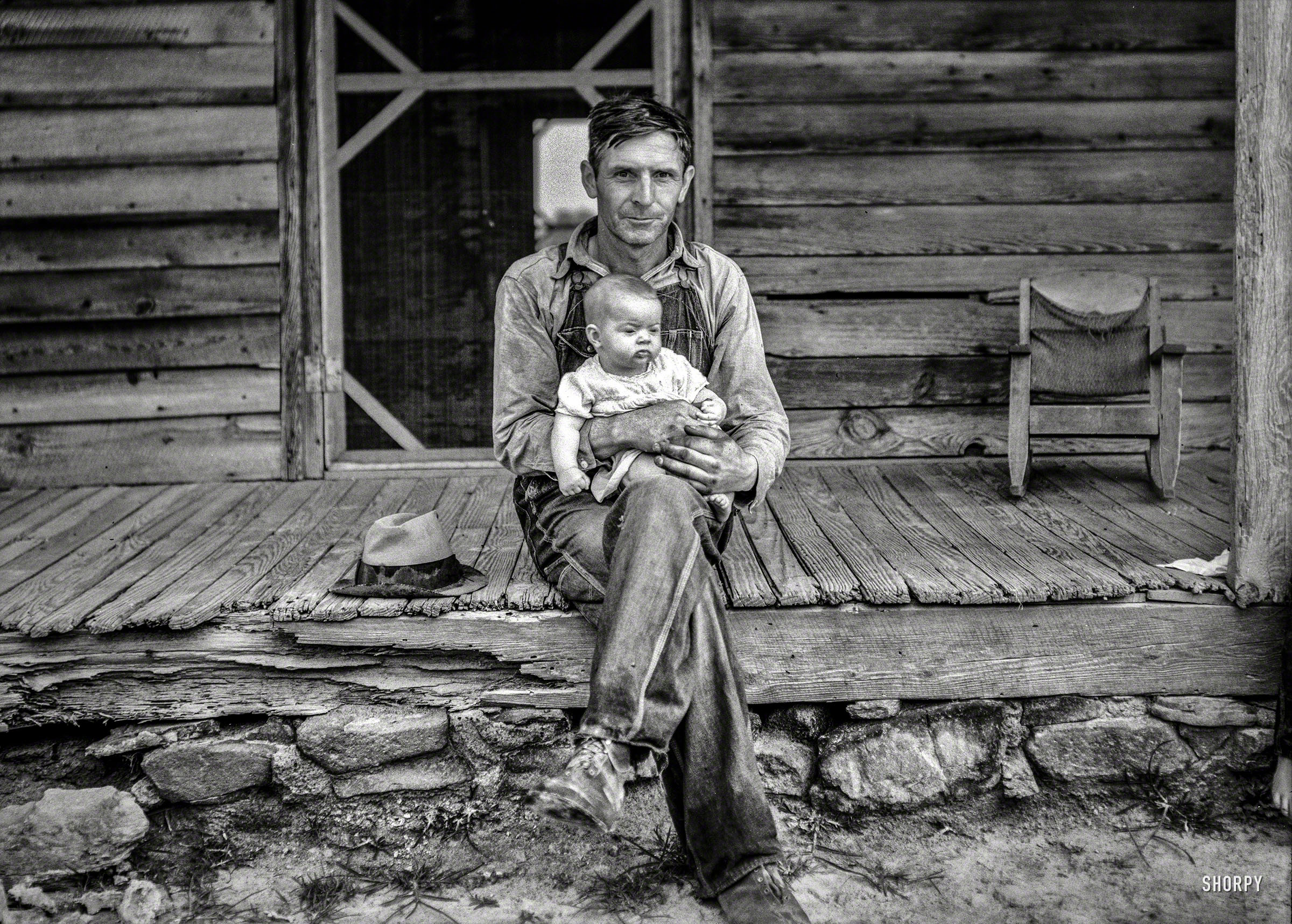 July 1939. "Mr. Whitfield, tobacco sharecropper, with baby on front porch. North Carolina, Person County, near Gordonton." Happy Father's Day from Shorpy! Photo by Dorothea Lange for the Resettlement Administration. View full size.
