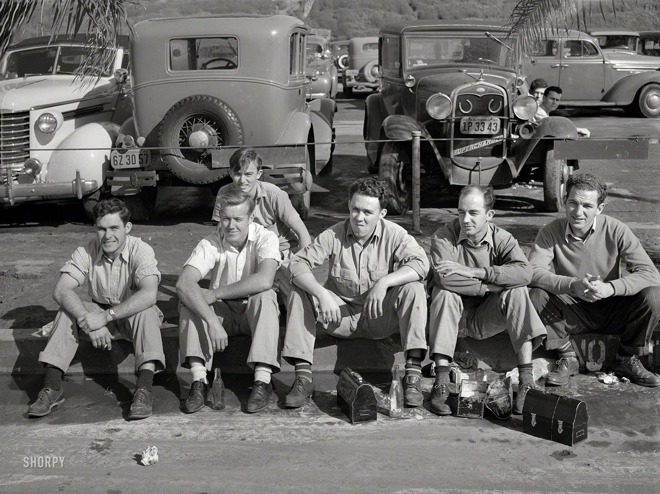 December 1940. "Workers eating lunch on curb across the street from the Consolidated Aircraft factory. San Diego, California." Medium format negative by Russell Lee for the Farm Security Administration. View full size.