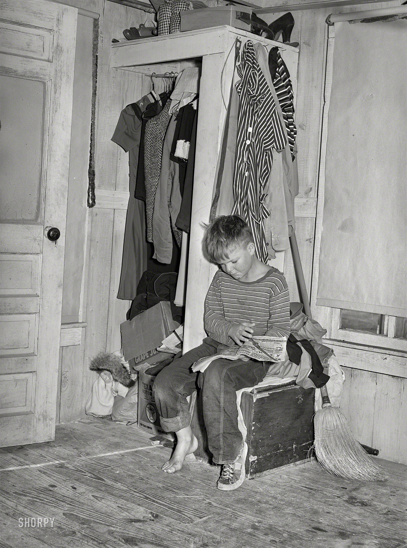 December 1940. Corpus Christi, Texas. "Small boy, son of carpenter from Hobbs, New Mexico, reading funny papers in corner of room in tourist court. Lack of adequate closet space is evident." Medium format acetate negative by Russell Lee for the Farm Security Administration. View full size.