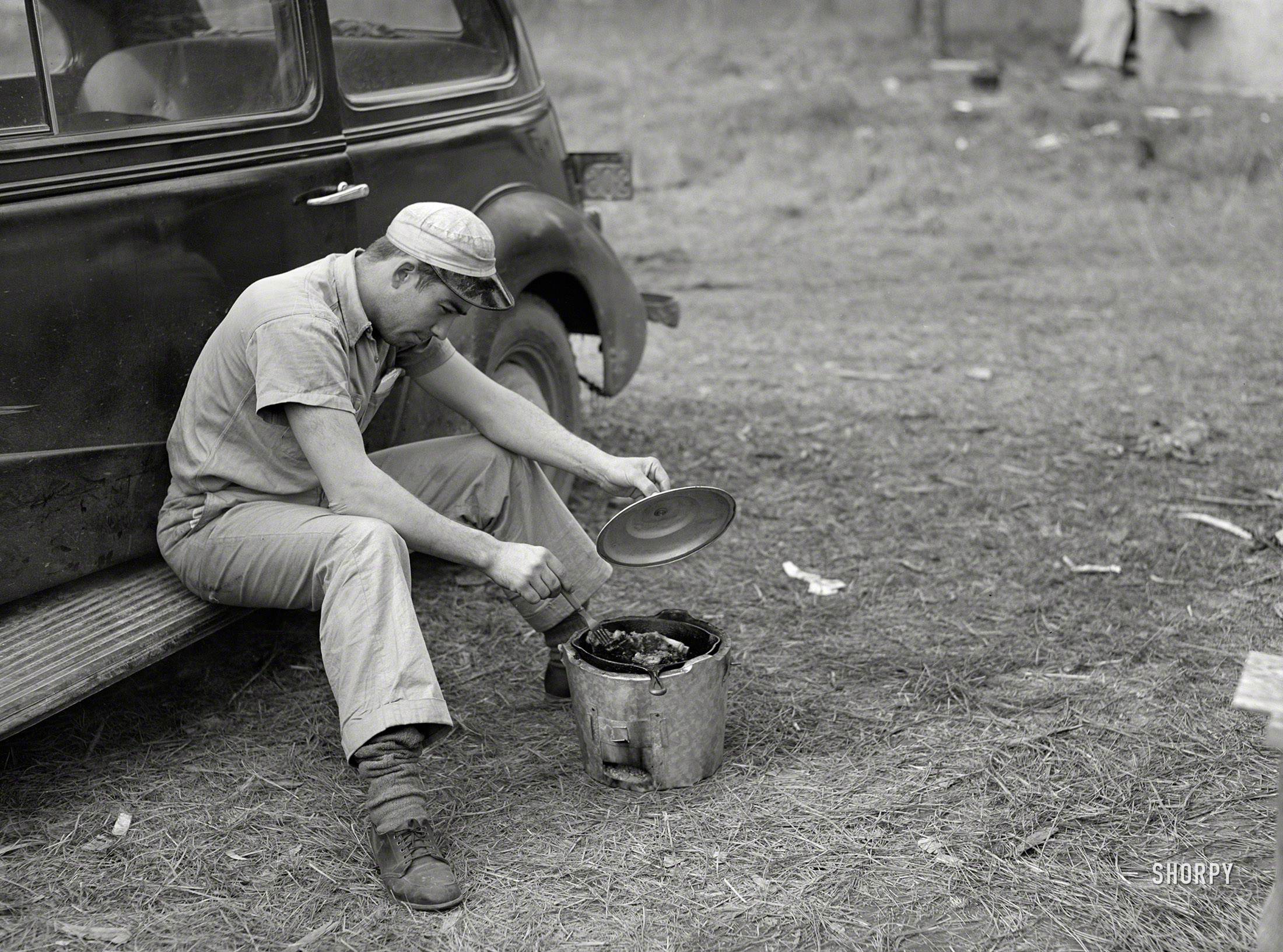 December 1940. "John H. Poole Jr. cooking while sitting on side of car. He is a carpenter on construction job at Camp Livingston. He comes from Monroe, Louisiana, where he has an electrical shop." Medium format negative by Marion Post Wolcott. View full size.