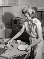 June 1941. "Wife of defense worker setting table for dinner in trailer home. Trailer camp at Erie, Pennsylvania." Medium format acetate negative by John Vachon. View full size.