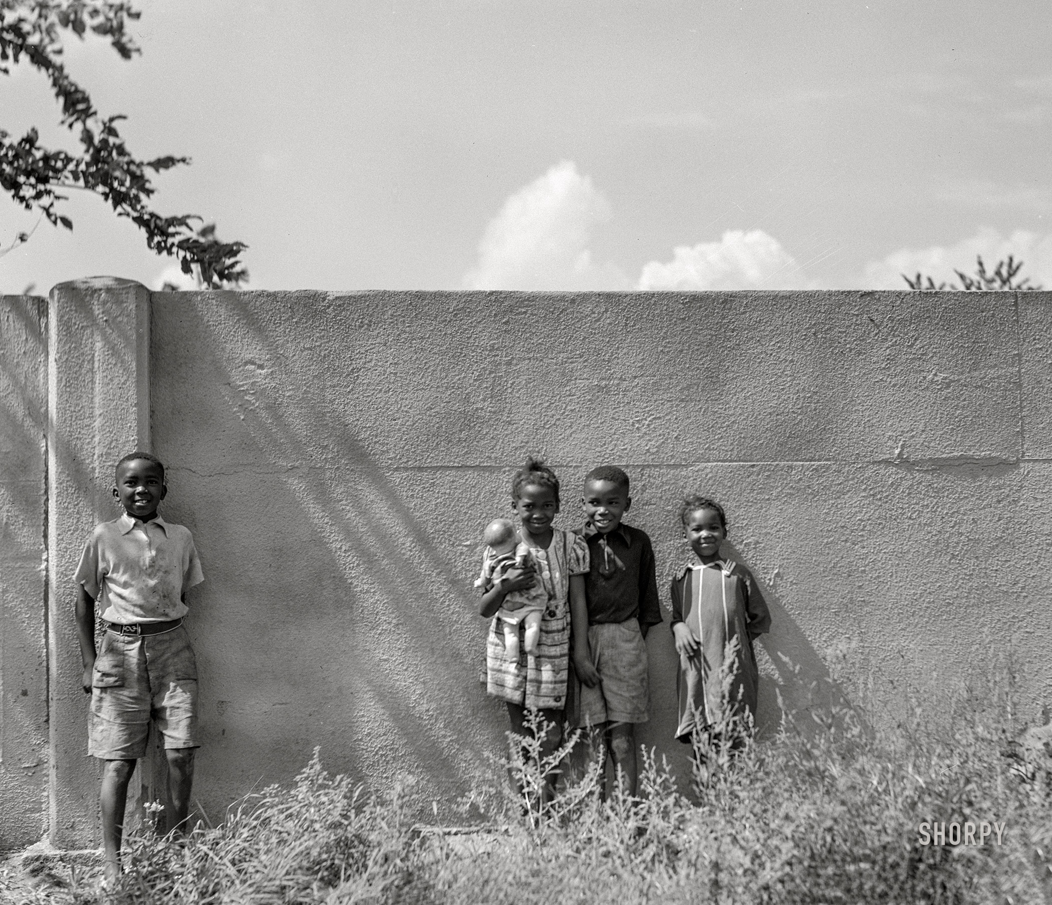 August 1941. "Negro children standing in front of half-mile concrete wall, Detroit, Michigan. This wall was built in August 1941 to separate the Negro section from a white housing development going up on the other side." Acetate negative by John Vachon. View full size.