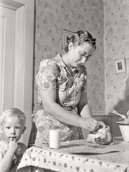 May 1942. "Lancaster County, Nebraska. Mrs. Lynn May, FSA borrower, cleaning a chicken." Our second look at this lady and that kid. Medium format acetate negative by John Vachon for the Farm Security Administration. View full size.