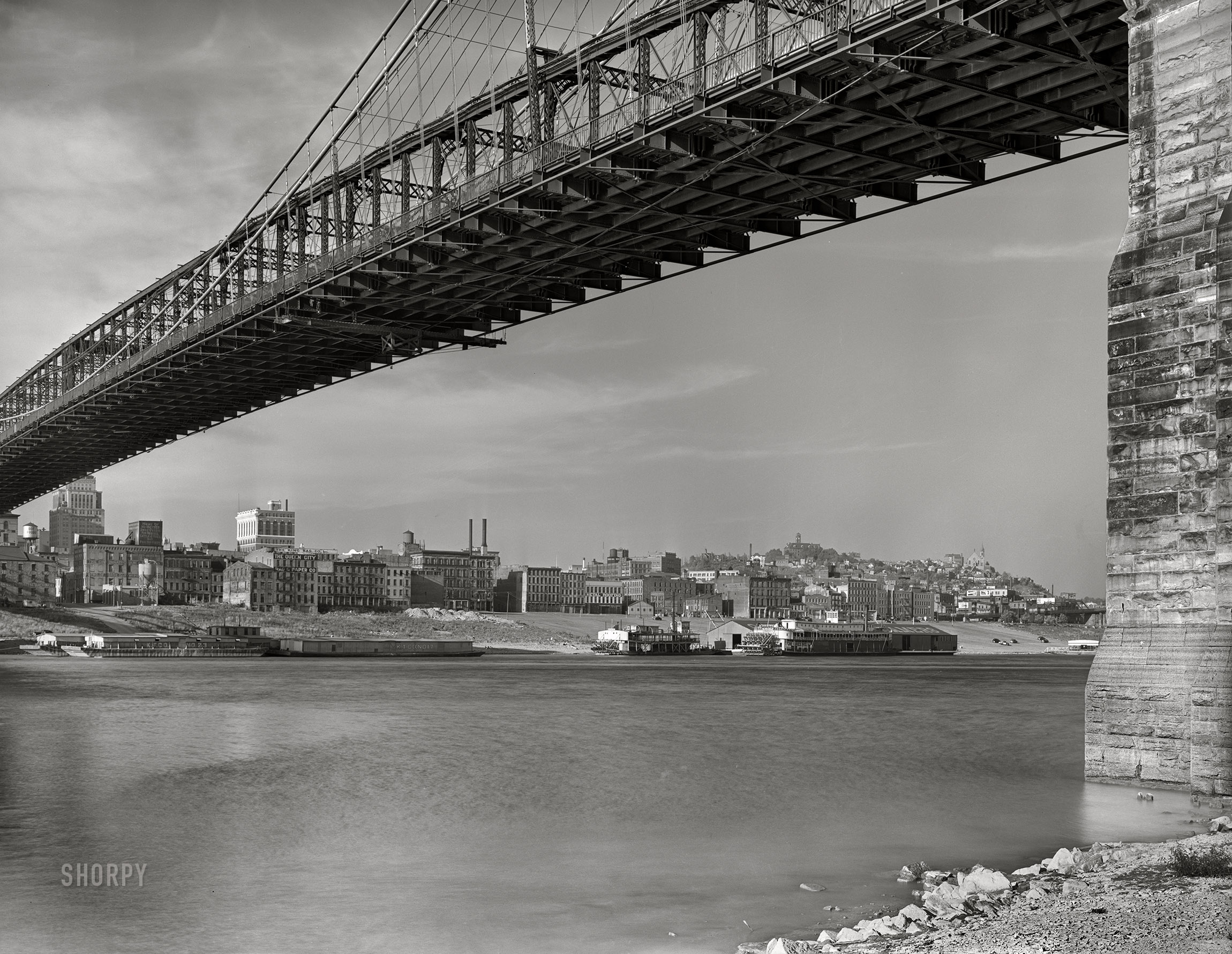 Spring 1941. "View under Roebling Suspension Bridge of Cincinnati from Kentucky side of the Ohio River. Waterfront showing numerous business houses: King Bag Company, Queen City Rag & Paper Company and others." 4x5 inch acetate negative for the FSA. View full size.