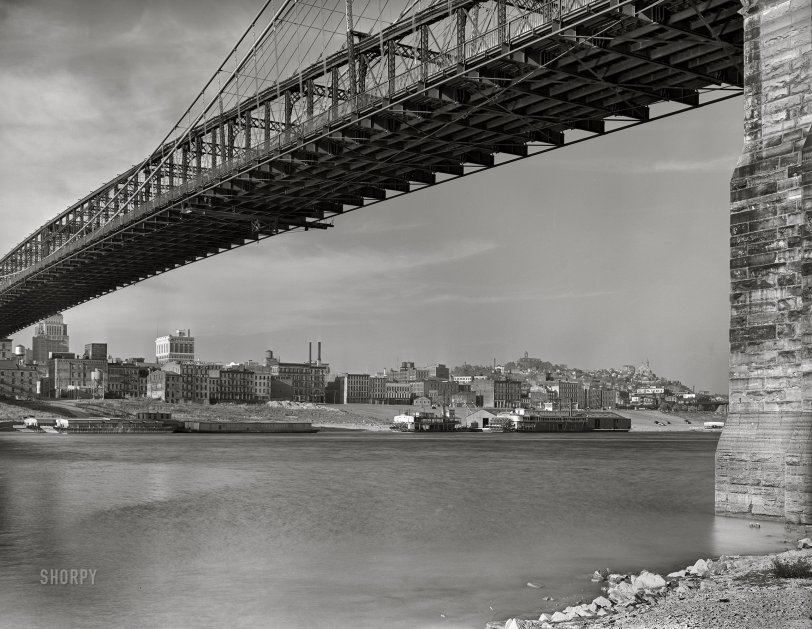 Spring 1941. "View under Roebling Suspension Bridge of Cincinnati from Kentucky side of the Ohio River. Waterfront showing numerous business houses: King Bag Company, Queen City Rag &amp; Paper Company and others." 4x5 inch acetate negative for the FSA. View full size.
