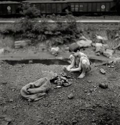 September 1938. "Coal miner's child breaking up large pieces of coal to take home. Pursglove, Scott's Run, West Virginia." Photo by Marion Post Wolcott for the Resettlement Administration. View full size.
Coal miners&#039; kidsThis was apparently very common in coal country in the early 20th century and before.  My mom was a coal miner's daughter born in 1910 in Bradenville, Pa. where her father worked the mines and she and her three brothers were often told to take burlap bags to the railroad tracks and pick up as much coal as possible that had fallen off the train cars as they rattled along.  They used it to heat their homes in the frigid Pa. winters and her mom would cook with it.  When I was very young and went there to my grandma's funeral, I well remember the miles and miles of the most train tracks I've ever seen and coal scattered everywhere.  We who are living today have no real idea of how very hard life was in earlier times.
He&#039;s going to look sharp in dress bluesWe grew up hearing the family was so poor that Grandfather would pick up coal off of the train tracks. Fast-forward 85 years, through the wonders of newspaper archives digitization: a 15-year-old Grandfather is arrested for picking up coal in the rail yard after he pushed it off of a rail car. The following month, Grandfather's name appears on a U.S.Marine Corps muster sheet at Marine Barracks Port Royal, South Carolina (now Parris Island). The beginning of the Sergeant Major's 40-year adventure.
Fred FlintstoneThe early years.
They almost arrested himthen they found out he had squatter's rights.
ShortsI had an outfit like that as a child. Get up, get in and that's it! 
Coal cars rumblin past my door...Both of my parents grew up poor in western PA "coal patch" towns. 
Every time I hear the song "The L&amp;N don't stop here any more" I think of the wonderful stories of the hard luck years they endured.  How I would give anything to be standing along the "sulfur crick" with rusty old Pennsy H21 and GLa hopper cars of coal (like those in the W Va picture) rumbling by. 
"I was born and raised in the mouth of the hazard holler...
Coal cars rumblin past my door..
Now they're standin in an empty row all rusty
And the L&amp;N dont stop here anymore" 
Not Only CoalIn the post-war 40's my brand new parents lived in a little rental house on a 15 MPH curve of the local highway.  Hundreds of produce trucks would make that turn every day - most at speeds exceeding the recommended 15 MPH limit.  This usually caused anything loaded above the top of the truck bed to roll off and into our yard.  Late afternoon would my folks and most others from the neighborhood gleaning the assorted veggies FOB.
Thrown in jailMy father got thrown in jail for picking coal off the tracks, Easter Sunday 1928. He was 15 - Delano, Pennsylvania.
Not just yesteryearSpringfield, Missouri has a coal fired plant and it is illegal to pick up coal along the tracks. Seems they had a problem with people getting too close to the trains.
Marion Post WolcottMarion Post Wolcott never seems to disappoint. She really had a great eye and fabulous technique.
Not just &quot;roadkill&quot;It was (and probably still is in the dirt-poor parts of the world) common to glean traffic lanes for "roadkill", so to say. The even harder version is people going though mine tailings for tidbits of coal, ore, or whatever may be useful. 
My dad recalls gleaning fields for wheat, rye, whatever ears the farmers' workers had lost or missed during harvest. 
[edit: not my best day, spelling wise ;-)]
(The Gallery, Kids, M.P. Wolcott, Mining, Railroads)