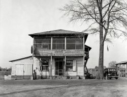 December 1938. "General store and post office, sawmill town. Ashepoo, South Carolina." Medium format negative by Marion Post Wolcott. View full size.
Ashepoo, South CarolinaThere is no longer a post office in Ashepoo, as the postal district was folded into nearby Green Pond in the 1960's according to the postal records.
I went back and looked at an assortment of USGS maps, and Ashepoo seems to have *never* been a large place.  Most of the houses that comprised the village seem to have succumbed to time and nature.
This is Ashepoo as it sits in modern times.  You can still see where the roads once lay, and while the view is far too distant to make any details out, the lone surviving building looks kind of familiar.
http://binged.it/1pPnMxF
NO TIN SIGNS!How on earth will I know which tobacco and soda pop to ask for. Is this so far off the track that even the Coca Cola people couldn't find it? 
The dark sedanWaiting outside the store is a 1933 Chevrolet Master 4 door sedan, the same model our family had in those years and drove west to Los Angeles to relocate from Independence Missouri in May, 1937. Many years later in 1963 my brother and I bought 1933 Chevrolet 2 door coach from a neighbor for $100 and kept it over 30  years.
Another sawmill townUntil I was about 11 years old I lived a few miles from Williams, SC in the early to mid fifties.  There was a large sawmill there, on the east side of Williams, and right across the road was a row of small houses owned by the mill company and occupied by the mill workers and their families.  I went to school with their children.  The mill once had a large fire that melted the tin roofs.  My father and I walked through the place after the fire and I picked up a glob of melted tin.  I kept it for many years.
A common sight throughout the south was large piles of sawdust left from temporary mobile sawmill operations.  After a period of time the sawdust would settle and develop internal air pockets, causing it to collapse if climbed on.  I know of at least one child that died that way. 
Ashepoo storeOwned by Benjamin Josephus Brant, died in 1946. See his gravestone on FindAGrave.com
http://www.findagrave.com/cgi-bin/fg.cgi?page=gr&amp;GRid=36433804&amp;ref=acom
Ashepoo DepooIt is/was on the Atlantic Coast Line RR main line (now CSX) between Charleston and Savannah.
The Brants of AshepooIt is entirely possible that the prop. of the General Store was also the railroad agent. I thought the name sounded familiar, and sure enough, there was a J. J. Brant, born 10 years before the photo of the store was taken, who was first trick Clerk-Operator at Yemassee (a few miles south of Ashepoo) when I hired out in 1973. I would not be at all surprised to find that J. J. was B. J.'s son, since nepotism was (and still is) a fully-acceptable and often-practiced tradition in railroading.
More info on the Brants...Michaelsjy:
Out of nosiness, I dug a bit deeper on Benjamin to see where he was before (and after), and to see what family he may have had.
He was born in Ulmers, in Allendale County.  Up until he appears in Ashepoo in the 1920 census, he stayed put in the Sycamore/Ulmers/Bardwell area.
He appears in 1917 in the WWI draft records as working for the "Berry Fortune Construction Company" as a bookkeeper.
I couldn't find him in 1920, but he appears running the general store in Ashepoo in 1930 and 1940, and Ashepoo was listed as his usual residence when he passed away in 1946.
Cause of death was stomach cancer that had spread to his liver.
In both 1930 and 1940 he was listed as a merchant, and his wife was postmistress for Ashepoo, a position she held until 1960.
There are no children listed in 1930, and in 1940 they have a 9 year old adopted daughter named Emma Jean Maddux listed as living with them.
WowEven the moss looks beleaguered.
Living up over the storeIt used to be (and perhaps still is)that business owners and their families in small towns would reside upstairs over their stores and this seems to be one of those instances.  I love the comforting presence of the two kitties making themselves at home and the screened-in sun room which lends a touch of hominess to the place.  As late as 1965 there was a very similar establishment just up the street from a second floor apt. which I was temporarily renting in a very small village in Ohio (New Knoxville).   The downside for the owner was that any time of the day or night, people who were in need of any given thing or service would pound on the door until somebody answered.  The upside was that your commute to work each day took no time at all.  Life was simple then.   
Fresh Chicken anyone?Also the chicken by the front door seems happy. Until lunch that is!
(The Gallery, M.P. Wolcott, Small Towns, Stores & Markets)