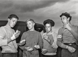October 1942. "Butte, Montana. Eating lunch at the scrap salvage campaign." Medium format acetate negative by Russell Lee for the Office of War Information. View full size.
ScrumptiousI'll bet those sandwiches tasted so good to the long-ago hungry, hard-working boys. I hope they got potato chips and a drink too, plus a giant oatmeal cookie.
Tasty"Golly, I sure am glad we were able to salvage these sandwiches from the trash!"
Wearing three hatsThe young man with facial hair is wearing what appears to be a chauffeur's cap.  There's a sort of name pin attached to the top, with a tiny bowler and top hat hanging down from it.  I can't read the pin.  Dave, can you please help?
Thanks Dave.  "Don't blow your top" is a phrase I haven't heard or thought of in a long time.  It's very Andy Hardy.
(The Gallery, Russell Lee, WW2)