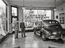 November 1942. "Lititz, Pennsylvania. Showroom of the Pierson Motor Company owned by Al Pierson, who is showing his one second-hand car to a local farmer. Before the war there always were three brand new cars in his showroom. Now the chief business of garages is repairing." Acetate negative by Marjory Collins for the Office of War Information. View full size.
Al Pierson at warMarjory Collins also photographed him sitting resignedly at his dealership desk. She reported that, in addition to keeping the garage open, he was working a defense job at Armstrong Cork Company in Lancaster, and serving as an air raid warden and aircraft spotter.

Hmmm. Rare photograph Usually the car salesman has his hand in the customer's pocket.
Spiel"This sweet thing was previously owned by a little old lady, who only drove it once a week to church -- "
Of light and colorThis is a good example of a photo often seen from this period that shows the position and number of flashes.  And it makes me think of how much equipment these photographers were lugging around, and how much effort they had to put into getting the shot.  Not to mention knowledge and skill.
Also, the car appears to be two-tone.  And I'm sure someone here can tell us what those two colors would have been.
Four Gallons a WeekThat "A" gas rationing sticker in the rear window allowed the owner to buy four gallons of gasoline a week.  Rationing wasn't done so much to reduce gasoline use as it was done to reduce use of tires and conserve the limited rubber supply.
I guess the farmer cleaned out the inventoryWe can see in the above photo that, in November 1942, Pierson Motor Co. had one used four-door car.  But the inventory was triple that in January 1943, as evidenced by the ad below in The Lititz Record-Express.  I also learned exploding antifreeze was a thing.
I found the ad looking for an address, which I guess Al Pierson felt wasn't necessary.  In another ad the location was listed as Main St.  I looked down Main Street on Street View and did not see a building like the one in the 1942 photo.
Reeling him in?Spiffy salesman appears ready to set the hook and close the deal on an attractive two-tone 1941 Plymouth Special Deluxe Sedan. A 1939 version from the same manufacturer is parked across the street.
Collins&#039; techniqueOkay, there are the shadows from the two flashbulbs -- but why are the farmer's head and right arm transparent, as if she had done open flash?
Brilliant new PlymouthInformation on Plymouth two-tone paint combinations for 1941 is minimal at best. Eye-catching color palette combinations can be visualized in period advertising, links below. 
https://vintagepaint.biz/images/source/Chrysler/Plymouth/1941_ply.jpg
https://i.ebayimg.com/images/g/VE4AAOSwSpZd1C7s/s-l1600.png
https://s.car.info/image_files/360/0-940480.jpg
RedefiningJail birds.
Tire treads?I don’t know anything about tires from this era, but the tire treads look a bit worn to me. Can anyone tell if they were in decent shape? Or during wartime, did we just take what we could get and save the good tires for the war effort?
Future military manI wonder what would happened to the young farmer. He seems to be of the age the military would mobilize for the war.  
Seems to be goneListed at 28 West Main Street, looks like a new fire department and a parking lot took over as usual.
Making ends meetAs GlenJay noted in the first comment below, Mr Pierson was holding down three jobs. But "serving as an air raid warden and aircraft spotter" would seem to be a cosy gig. As we all know, in 1942, swarms of German bombers made repeated non-stop transatlantic return flights of 40 hours  in order to disrupt the operations of the Armstrong Cork Company, a key part of the US weapons industry. Seriously, who in government was that far out-of-touch that a ridiculous position of air raid warden and aircraft spotter was funded in nowheresville Pennsylvania?
My dear departed mother was an incendiary bomb rooftop spotter in Oxford, England during the 1940/31 Blitz. For some reason, Germany never bombed Oxford despite the huge Morris Car factory churning out Bren Gun Carriers. But German bombers regularly flew over Oxford on the way to Coventry. Kept her watchful. All Mr Pierson ever had to do besides filling out forms full of zeroes in the Qty columns every day, was to have a darn good sleep every night and collect a paycheck now and then. Truly farcical and illogical to have such official positions, but governments wanted people to be in constant fear of armed alien hordes invading their one-horse towns, apparently. Still at it today.
Light and DarkSeems this image was edited in the darkroom to balance light and dark areas, outdoors and indoors, but not consistently edited. Look out the window on the left, there is a straight vertical strip almost the full height of the window where the house and the trees are all lighter within that strip and darker on both sides outside the strip. Light and dark editing would also explain farmer's transparent effect. Probably not a flash or other artifact, just darkroom work. They could do a lot in the darkroom before Photoshop.
[There was zero editing "in the darkroom." This is a scan of the camera negative. - Dave]

Re: technique, and paint colorsI googled "1941 Plymouth Special Deluxe Sedan colors" and was surprised to discover how many possible colors this car might have been.
I'm also surprised that no one has commented on the gas thief bird cage.
As for the partially transparent farmer, I think I have a plausible explanation.  The most obvious and visible image we see of him is the result of the exposure during the flash.  But the film was exposed for a longer duration than that, in order to fully capture the outside elements, and during that time, he moved the parts of his body that appear to be a double exposure (his right arm and the back of his head).
Reminiscent of 2020-22The idea of one used car in a dealership is reminiscent of what we saw during Covid, when supply chain was so badly constrained. 
I recall showing up at the local Subaru dealer for service and they had absolutely nothing on the showroom floor. No new cars available, and few used. 
Third brake/tail light Didn't realize they had that back in the 40's . Thanks !
Lively ACIntrigued by the bird cage with its catchy sign, I did some digging.
An online auction listing for a bird cage similar to this one but plugging (haha) AC spark plugs describes it as a "Vintage Gas Station Display/Sign. Nice early Spark Plugs Display consisting of two old spark plugs posing as birds in a bird cage with a double-sided tin sign hanging underneath that reads: 'These Birds Were Caught Stealing Gas! And replaced with Lively AC spark plugs' The early ones did not have the AC brand on them; they did that later."
So it seems that our sign is one of the early ones without the branding. Now I just wonder why it appears that there is a single stuffed bird in the cage, and not two spark plug birds. Maybe those flew away.
The wall hanging (not the car)Your next car _ De Soto.  Styled to stand out _ Built to stand up!
(The Gallery, Cars, Trucks, Buses, Marjory Collins, Small Towns, WW2)