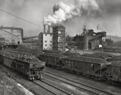 November 1942. "Pittsburgh, Pennsylvania (vicinity). Champion No. 1 cleaning plant. Loaded coal cars ready for market." Photo by John Collier, Office of War Information. View full size.
*cough*This is why nobody cared if they smoked cigarettes back then. 
CLEAN coal???This has nothing to do with modern claims of cleaner (less polluting) coal. I did some research and this is about cleaning the dirt and detritus from the dirty coal. It looks cleaner but still burns dirty!
Anthracite coal sizesI was intrigued by the different sizes of coal in the various cars, so I looked it up and discovered the following (from smallest to largest, by name of size):  barley (size of coarse sand), rice (pencil eraser), buckwheat (dime), pea (quarter), chestnut (golf ball), stove (baseball), and egg (softball).  But I’m still a bit confused because those chunks in the cars on the left are certainly bigger than softballs.
This is not anthracite (hard) coal. This is bituminous (soft) coal, a higher sulfur coal -- smokier and more ash. There were different grades of soft coal, and this is most likely from the West Kittanning B seam. A very high heat to ash coal. The steel mills just ate this stuff up. Soft coal was mined in the western part of Pennsylvania along with West Virginia and Kentucky down the Appalachians, hard coal specifically to eastern Pennsylvania.
Coal sizesI'm old enough to remember steam locomotives.  A branch line separated two sections of my grandfather's farm, and I recall picking up huge chunks of coal that fell off overloaded tenders, some of them easily 12 inches or more in diameter.  Coal was the common fuel in those days, and we used stove coal in the furnace.  The water heater was fired with pea coal. 
(The Gallery, John Collier, Mining, Pittsburgh, Railroads)