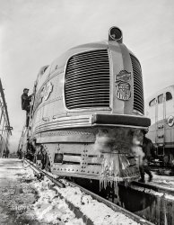 December 1942. "Chicago, Illinois. One of the Chicago and North Western Railroad streamliner diesel electric locomotives. These trains are operated jointly with the Union Pacific Railroad to the West Coast." Acetate negative by Jack Delano, Office of War Information. View full size.
Not hybrid or EV.Locomotives are diesel-electric, not hybrid. The electric part is the method of power transmission between the engine and wheels because they have a 250-950rpm operating range. A gearbox would be too large and complex to be practical, especially when synchronizing multiple units. They don't charge or operate on batteries (except some at low yard speeds for shuttling).
[You're thinking about this much too narrowly. Hybrid: "Of mixed character; a thing made by combining two different elements." - Dave]
Ice BeardJust like old man winter.
Chug and playShorpy is certainly correct - but then almost all (North American) "diesels" are such: a diesel engine drives a generator that powers the traction motors. But the U.P. was strictly an amateur about combining powering methods

The SBB lok is still around - ! - but converted back to free-range capabilities.
EMD E6It looks like the EMD E-series, guessing E6, built from 1938 to 1942.
I take it backThe E-series didn't have the radiator.  Lionel offered two streamliners, the M10000 and this thing.  I can't find pictures of this thing that also give the model number.
Achoo-choo!It looks like its nose is running!  I love that streamlined look, though.  I'll bet it's sporting that striking Union Pacific armour yellow and gray paint scheme, too! 
Re: Achoo-choo!You are absolutely correct!
Not an E-unit. It&#039;s an M-10000!I think that the "runny nose" comes from water in the air hoses. (Just a guess!!)
(The Gallery, Chicago, Jack Delano, Railroads)