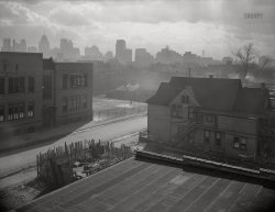 February 1942. "Detroit, Michigan. Looking towards downtown from the slum area in the early morning. These are conditions under which families lived before moving to the Sojourner Truth housing project." 4x5 acetate negative by Arthur Siegel for Life magazine. View full size.
Good ol&#039; days?Clean white curtains in the school house windows, and no trash strewn in the streets. Air looks terrible -- all those factories I guess.  Those are mostly gone now.  While the house in the lower right looks dilapidated, it looks better than much of Detroit did for many years, perhaps until recently.  
None were so blind(ed)Every school I ever attended used venetian blinds;  I've passed by some that use shades, but have never seen one that used curtains for its windows (what a genteel time ... long gone!)
The juxtaposition of buildings on the skyline - Hudson's to the right of the Penobscot Building (and the Book-Cadillac even further right) tells us this is northeast of downtown, though perhaps not as far out as the mentioned Sojourner Truth Homes (the full name of the school remains tantalizingly just out of reach). This appears to be Adelaide Street, the school - Bishop - was a noted landmark, tho the orginal building had burned in 1936. (Curiously, despite the area being frequently targeted for slum clearance, the school, as well as the buildings in the foreground, endured until c. 1970, surviving even a freeway ramp that ran next door..literally.)   The SJTH were just opening when this was published, not without headlines (of the wrong kind.) 
Sojourner Truth riotThis photo turned out to be cruelly ironic: the attempted relocation of Black residents was met by a clash between White opponents and Black supporters. The resulting "Sojourner Truth riot" led to 220 arrests -- with 109 charged, only three of them White. Settlement of Sojourner Truth was halted, leaving many of those moved from the slum Siegel photographed with no place to live -- doubly displaced. Detroit then mandated segregation in public housing, with "racial patterns of a neighborhood" not to be altered. Sixteen months later came the Detroit race riot of 1943.
Air Quality?This view is looking north, and just beyond the downtown office buildings and hotels there is the Detroit River. Windsor, Ontario is on the other side of the border, and I grew up there in the 1950s. I had evening swimming lessons at age 9 in the winter of 1956 at the Windsor YMCA. Afterwards we had a snack at the Chicken Court next door. When I emerged from the Y there was a strong sulfur aroma in the cold night air from the use of coal for industry and home heating. 
(The Gallery, Arthur Siegel, Detroit Photos)