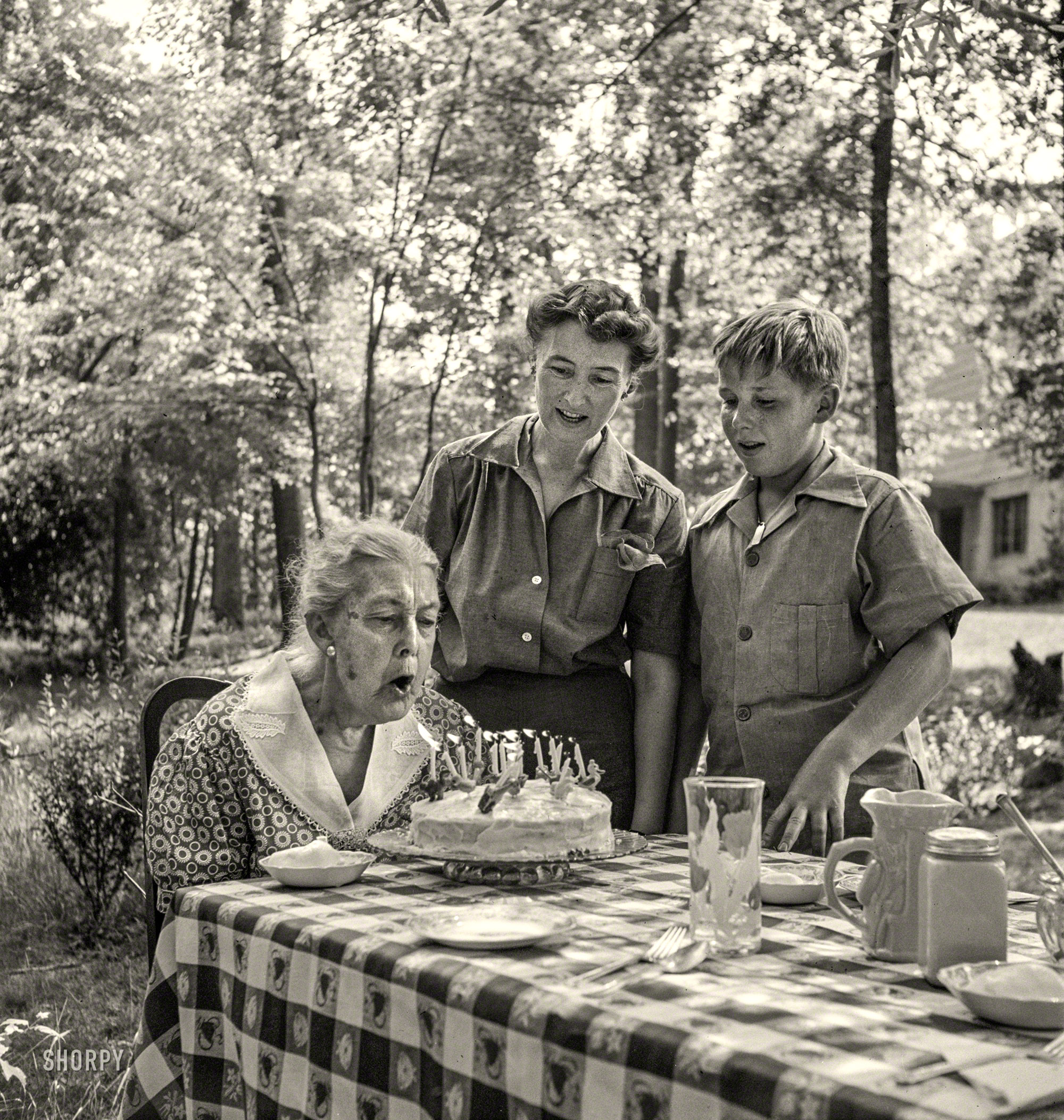 June 1942. Greenbelt, Maryland. "Grandma Taylor blows out the candles on her 83rd birthday cake while her daughter, Mrs. McCarl, and grandson look on." Photo by Marjory Collins for the Office of War Information. View full size.