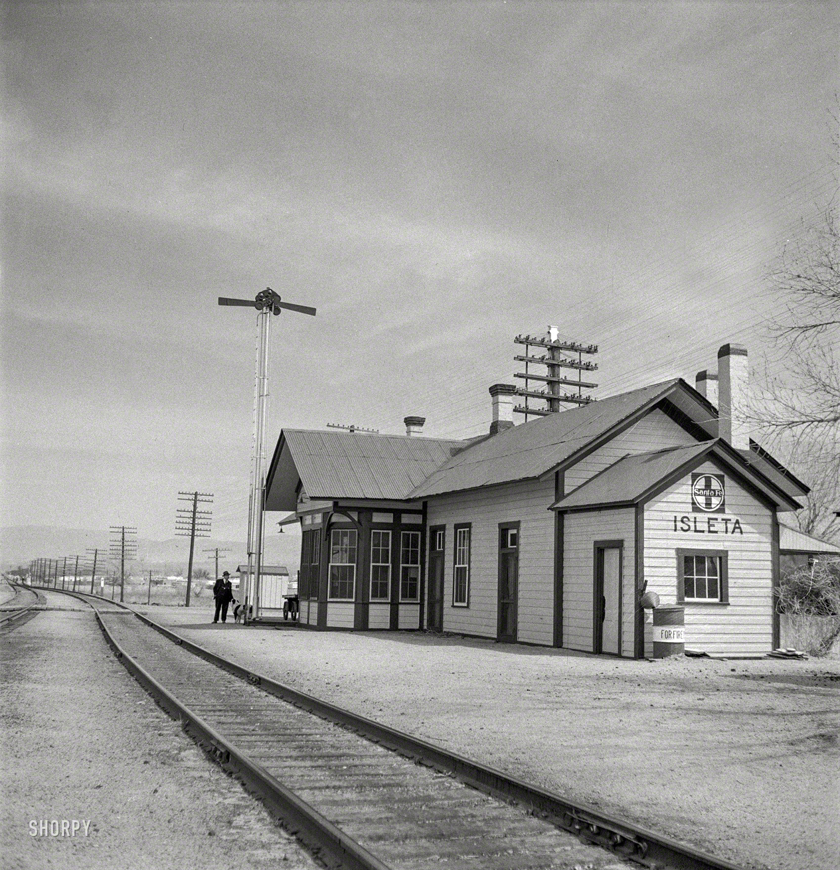 March 1943. "Isleta, New Mexico. The Santa Fe depot. Horizontal arms on pole indicate a 'red beard,' that is a message is to be picked up by the train crew." Photo by Jack Delano for the Office of War Information. View full size.