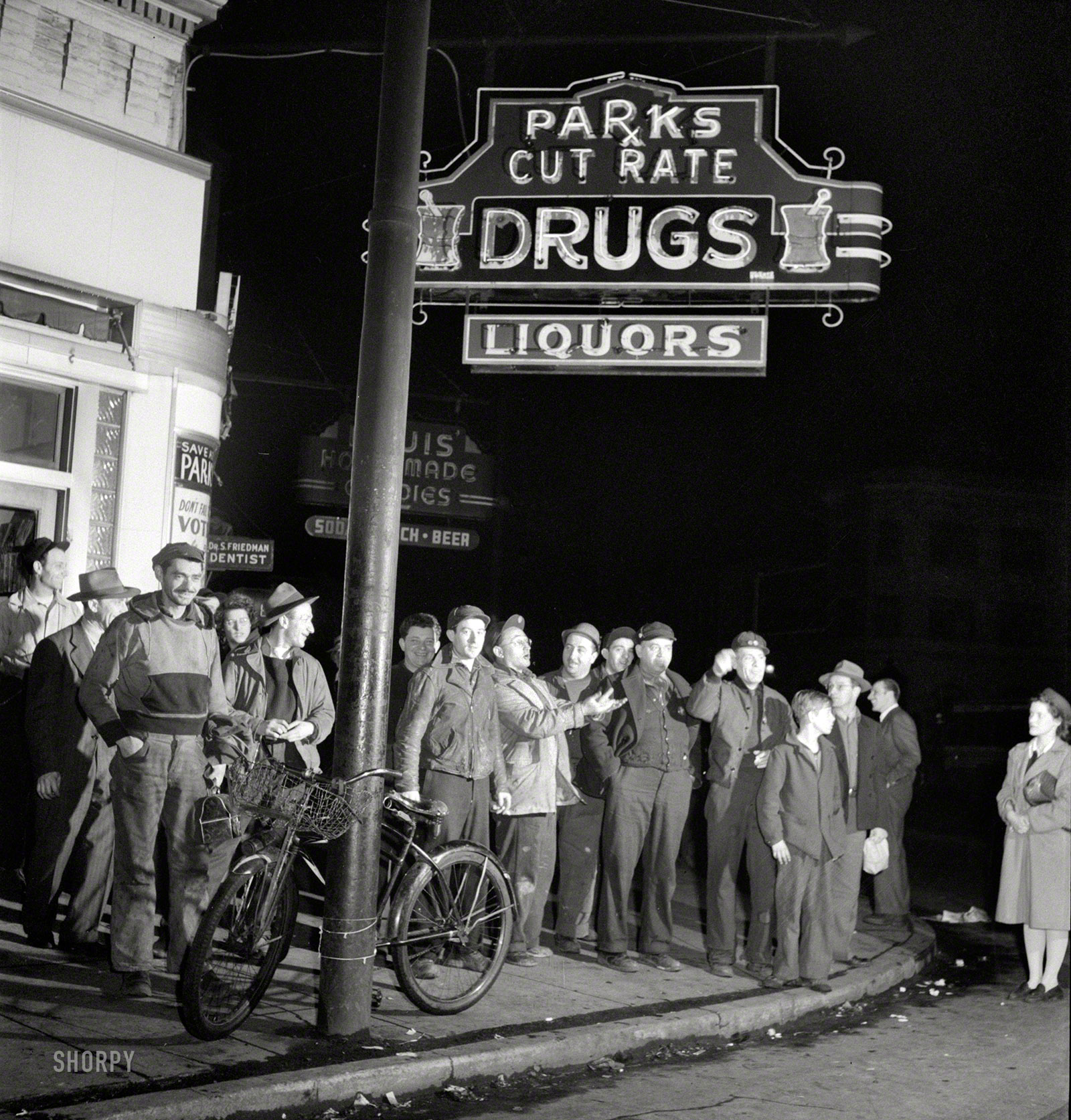 April 1943. "Baltimore, Maryland. Third shift workers waiting on a street corner to be picked up by car pools around midnight." Last seen at the lunch counter. Photo by Marjory Collins for the Office of War Information. View full size.