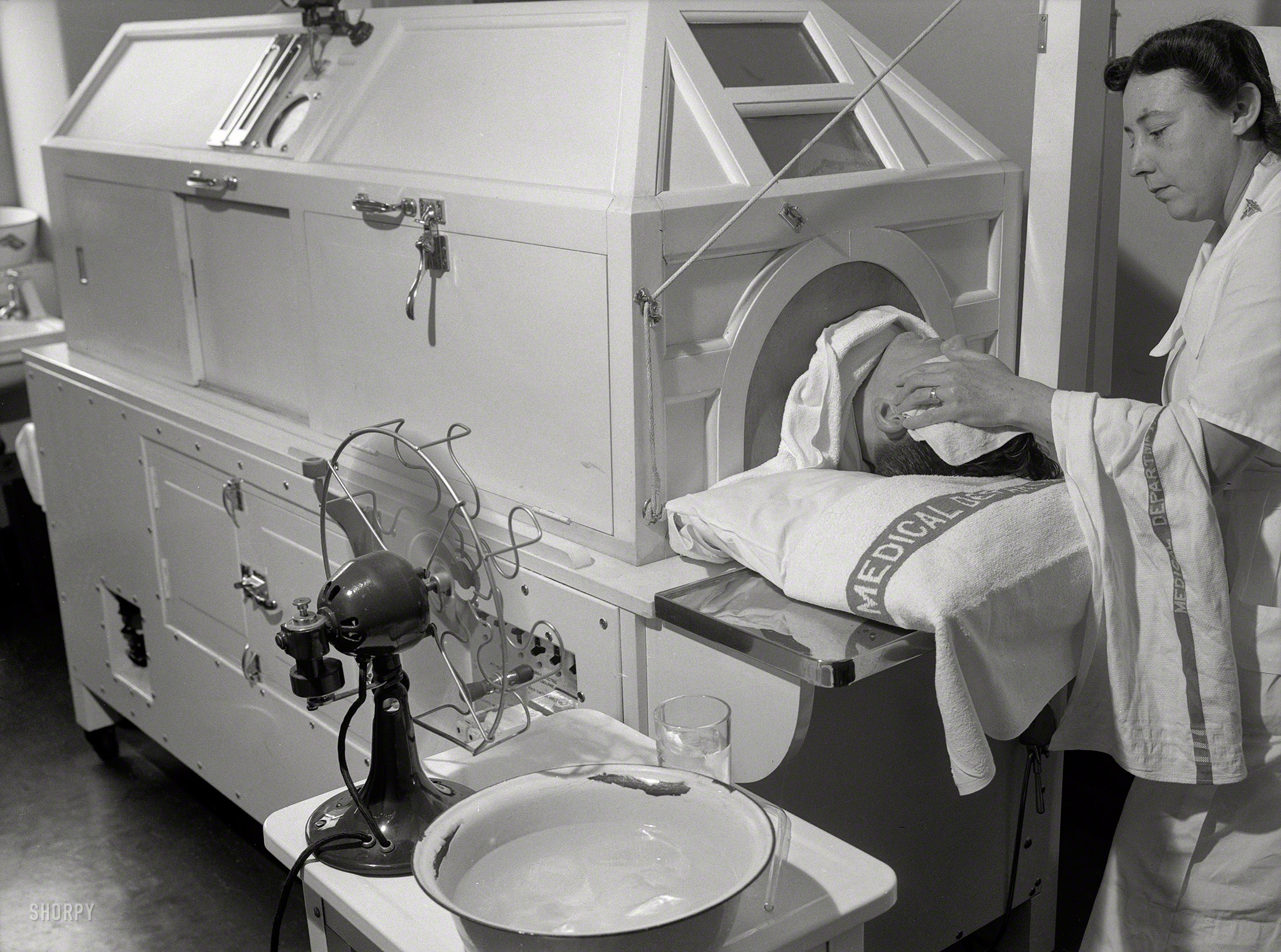 1943. "Melbourne, Australia. United States Army hospital. Patient receiving treatment in new fever machine which keeps temperature at 107 degrees (108 degrees is fatal). Note ice in basin and fan to cool head." Photo by Jo. Fallon for the Office of War Information. View full size.