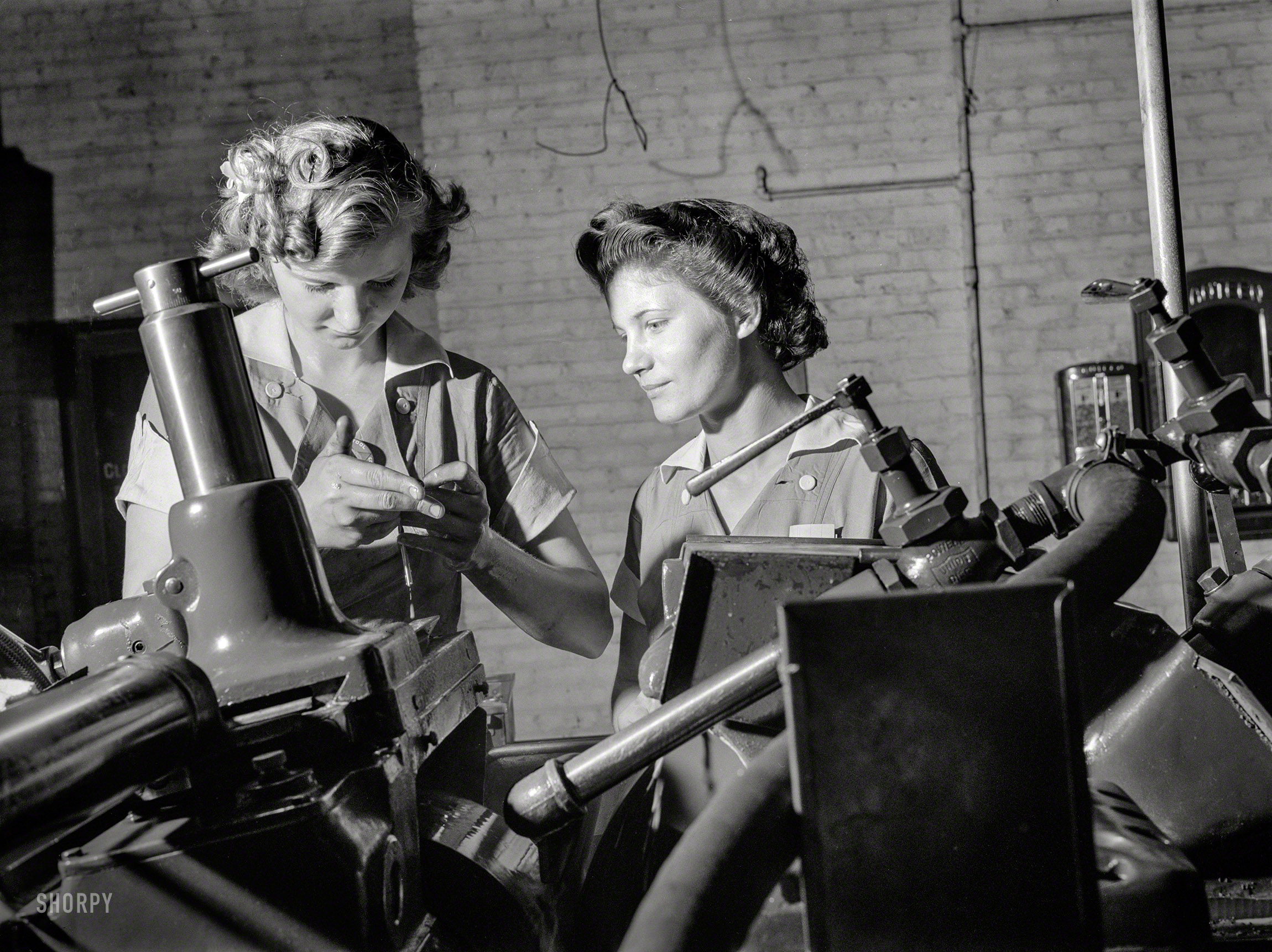 August 1942. Republic Drill and Tool Co., Chicago. "Pioneers of the production line, these two young workers are among the first women ever to operate a center&shy;less grinder, a machine requiring both the knowledge of precision measuring inst&shy;ruments, and considerable experience and skill in setting up. In this Midwest drill and tool plant, manned almost exclusively by women, centerless grinders have been efficiently operated by women for more than a year, and company prod&shy;uction figures have continued to soar." Medium-format nitrate negative by Ann Rosener for the Office of War Information. View full size.
