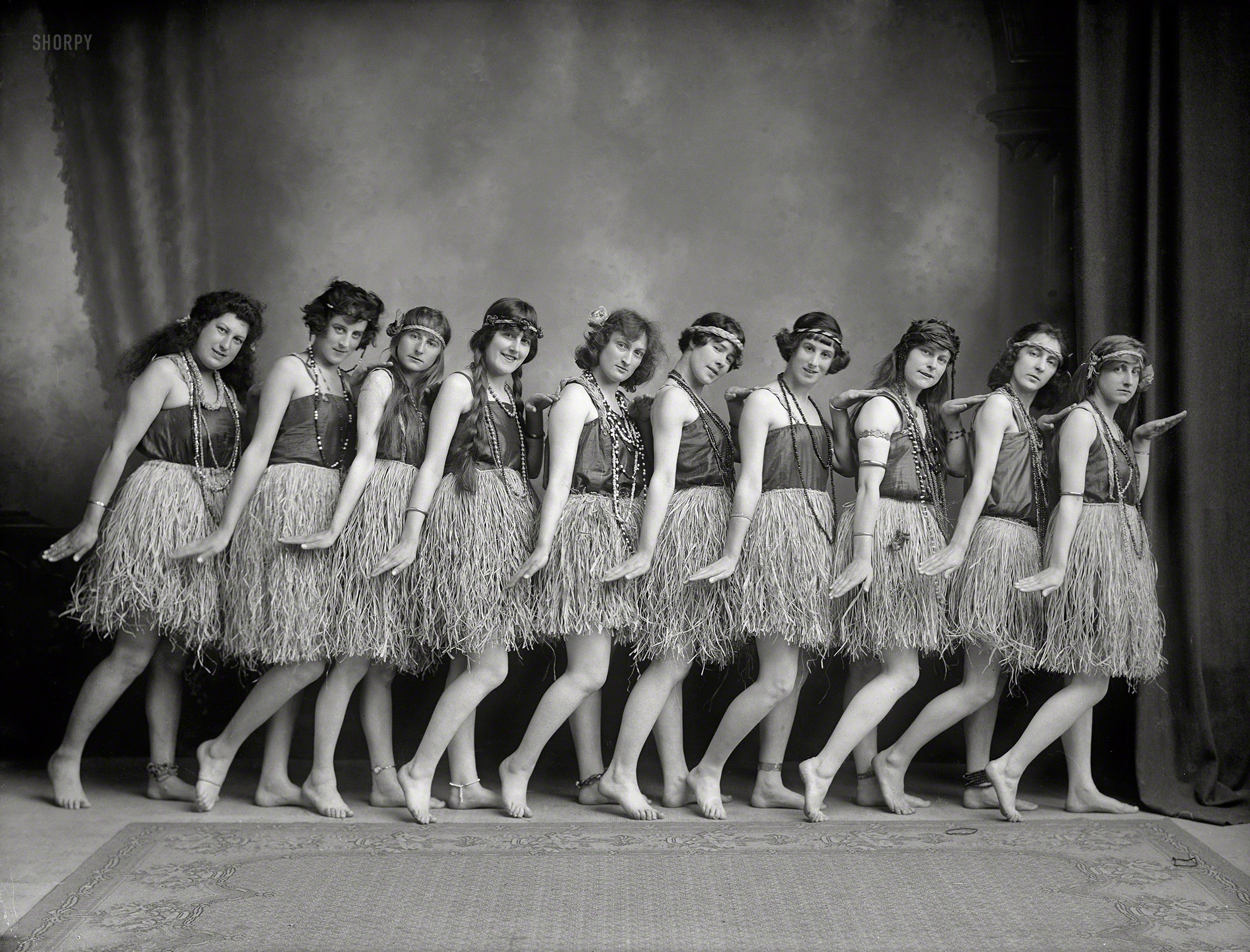 Lasses in grasses circa 1920s. "Nelson District, New Zealand. Row of young women (music hall dancers?) in costume, standing barefoot in dance pose, wearing headbands, long strings of beads, Hawaiian hula style grass skirts and anklets." Glass negative by Frederick Nelson Jones. View full size.