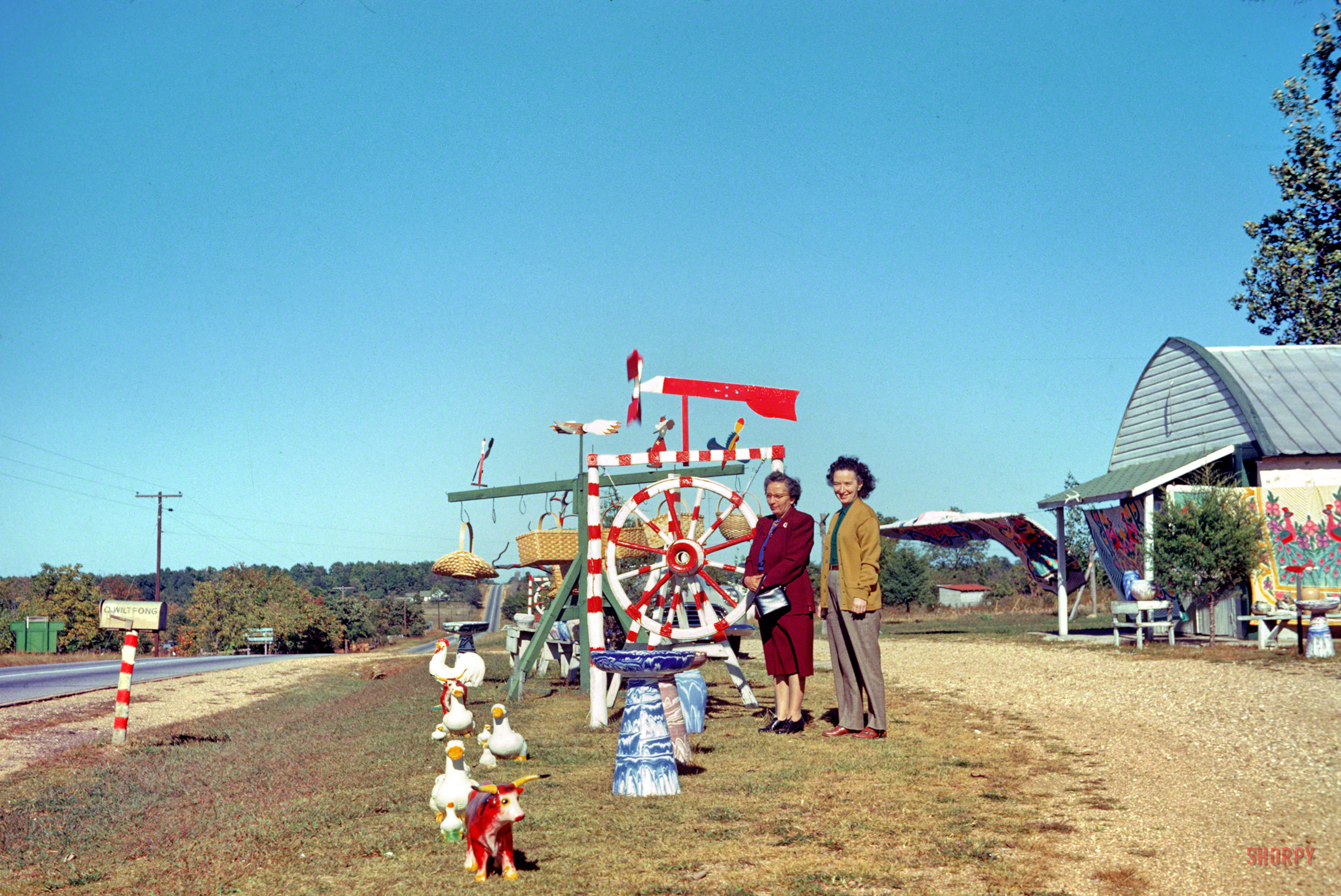 "6 Oct 1952. Clara & Grace at chenille & souvenir shop south of _______ ." We're back with Hubert and Grace on their road trip from Minnesota, the day before our previous photo was made at Eureka Springs, Arkansas. Where are we now? 35mm Kodachrome by Hubert Tuttle; paint by Dr. Seuss. View full size.