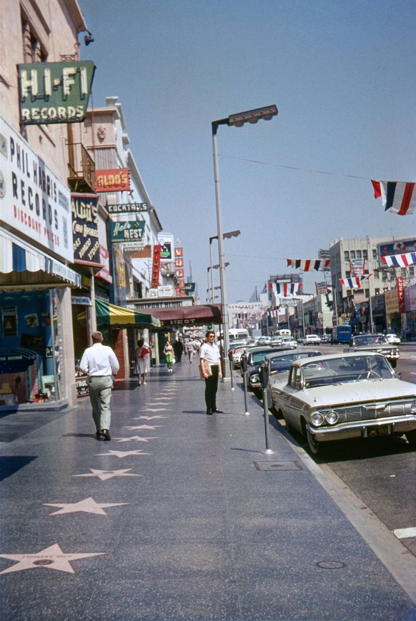 August 1963, Hollywood Boulevard. On "The Walk of Fame." My brother, standing down the block in the vicinity of the '61 Chevy, holds a bag of records, so we've just come out of Phil Harris Records on the left. No relation that I've been able to determine, but a notable Hollywood establishment nevertheless. Another is down the street: Frederick's. Nearest star is for early Hollywood pioneer Thomas Ince, a name definitely worth a Google. View full size.