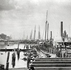 Circa 1865. "City Point, Virginia. Unloading Federal supplies from transports." Civil War glass negative collection, Library of Congress. View full size.
Walking Beam EngineLove the walking beam engine on the Columb(ia?). I have always been impressed with how large they were.
Primitive logisticsIn examining this photo, it is useful to remember that the Federal army was operating in enemy territory; that the South's infrastructure had deteriorated; and a line route for the railroad was not available because Richmond had not been taken.
 I suspect the size of the shipping was dictated by the James River and the decay of the docks.
I have not seen a good book on the logistics of the Civil War. Perhaps someone could suggest a title?
General George Gordon MeadeI apologize if my English is not very good. I'm from Cádiz (Spain), where General George Gordon Meade was born in 1815. I am very concerned for his involvement in the American Civil War (it was a bit controversial) and especially by his father, Richard Worsam Meade, who died in 1828 in Philadelphia. Richard Worsam Meade had a large fleet of boats in Cádiz, but lost everything in the war against Napoleon for his generosity to the Spanish cause. Was imprisoned in the Castle of Santa Catalina in Cadiz due to debts contracted. When he was released back to the United States.
Technology Moves SlowlyAs in previous views of City Point (now Hopewell, VA, it appears from modern maps), one is struck by how primitive the operation was considering it was the main front in one of the biggest wars in US history.  Contrary to the impression from history books, most of the logistsics ships are sail rather than steam (and this is some 50 miles up the James River from its mouth -- much more efficiently handled by a steam ship).  On land, it's draft animals pulling wagons, not railroads, although the latter were common in the time period and actually did play a role at City Point.
Another peculiarity is the ramshackle appearance of the infrastructure -- no neatly organized piers with cranes on them, as we would expect in more recent conflicts, but a maze of pilings separating the berths for the ships from the shore, with no obvious way to get the cargoes across the shoals but lighterage, and what might be the decking of a pier being laid in the foreground.
I think the railroad was operatingIt can bee seen in the background of this shot https://www.shorpy.com/node/17027
(The Gallery, Boats & Bridges, Civil War)