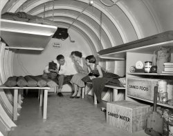 1955. "H-bomb hideaway. Family seated in a Kidde Kokoon, an underground fallout shelter manufactured by Walter Kidde Nuclear Laboratories of Garden City, Long Island." United Press photo. View full size.
How much lead lining?Without any lead lining, and depending on how deep the shelter was buried, this wouldn't do you much good.
[Not true. Three feet of packed earth above the shelter will reduce the intensity of gamma radiation by a factor of 1,024. - Dave] 
Dave, I'm not sure about the factor of 1024 you speak about.  In reading this information, there is a level of protection in a small amount of dirt or concrete.  Of course, if you don't insulate the door, your shelter won't get a glowing report; but you will.  I've also read that many early bomb shelters were built less than 12 inches below ground level, and some were just placed in a basement.
[The standard minimum 3-foot depth for an effective earth-shielded fallout shelter is based on well-established research. This is why underground shelters don't need a lead lining. - Dave]
A basic fallout shelter consists of shields that reduce gamma ray exposure by a factor of 1000. The required shielding can be accomplished with 10 times the thickness of any quantity of material capable of cutting gamma ray exposure in half. Shields that reduce gamma ray intensity by 50 percent include 1 cm (0.4 inch) of lead, 6 cm (2.4 inches) of concrete, 9 cm (3.6 inches) of packed earth or 150 m (500 ft) of air. When multiple thicknesses are built, the shielding multiplies. Thus, a practical fallout shield is ten halving-thicknesses of packed earth, reducing gamma rays by approximately 210, or 1,024, times.

deja vuSome years ago in Seattle after retiring to the backyard after dinner with a new friend I noticed a wheeled hatch in the middle of the yard. "Oh that's our bomb shelter" the host exclaimed, and sure enough after she opened the hatch we all went down a ladder into a shelter looking exactly like the one pictured. It even had a couple of unopened crates of (50 year old) canned goods still piled in the corner. A very weird deja-vu to say the least since I distinctly remember them being sold off parked flat bed trucks near my neighborhood as a kid.
What&#039;s missing?I see canned food. I see canned water. Where's the can?
Space efficiencyYes, by all means, let's take up valuable space by keeping the canned food and water in cases made of 3/4" plywood!
Lulz-deficientThey forgot the canned laughter.
Brilliant design, business dudThat radiation monitor is an extremely clever device that works entirely without batteries, which in other radiation detectors of the time were typically in the depleted state when you finally needed them.
And it was total business flop.
Walter KiddeWas this the same company that makes firefighting equipment?
Half-thicknessA substance's ability to shield from radiation is measured in half-thickness, which obviously is the amount of material needed to reduce the radiation dose by 50%. It also depends on the radiation source, for example cobalt-60 is more energetic than cesium-137 and therefore requires a thicker shield to get the same reduction.  I couldn't find anything for packed earth, but the half-thickness for steel with a Cs-137 source is about half an inch.  Several feet of packed earth would definitely reduce the radiation level, probably by quite a lot.  Without more research I can't be sure how much.
[The half-thickness for packed earth is 9 cm, or 3.6 inches. Multiplying that by ten, to 36 inches, reduces radiation by a factor of 210, or 1,024. - Dave]
Twilight Zone episode?I don't foresee a happy outcome here. It's going to get weird any minute.
Playtime?Little Girl has her toy stuffed cat to play with, so I guess Mom  &amp; Dad will be fighting over who gets to play with the toy Jeep on the floor!
Where the elite shelter.Seriously, I lived through this era (born in 1942), and nobody had one of these.  They were seen in newsreels, and PR photos like this, but no real family wanted, or could afford this nonesense.  
Necktie Geez if I'm going to have to wear a necktie I'm not going.
Where&#039;s Junior?I see a toy Jeep partially visible behind the box of canned water.  Did Junior not make it in time?
Kanned HeatIn your Kidde Kokoon you will have Kanned Water, Kanned Food, and Kanned Heat!  (aka: Sterno)
D.I.Y.Did the owners of the shelters have to furnish the interior to suit their needs. Those shelves and bunks look fairly homemade.  What a gloomy place.
I&#039;d rather be deadLiving in this thing with my family would be worse than the alternative. We'd be at each other's throats in a few hours. 
If you're going to have a bomb shelter, at least make it comfortable!
Chocolate DropSpam and sweet cocoa for sandwiches and cocoa cupcakes. It's a lifestyle.
Are You Kiddeng Me?I hope there are closed-environment sanitation facilities/provisions out of camera view. Otherwise, it will be a foul smelling and unsanitary Kokoon before too long.
US Army Trenching ToolKind of curious to know why they have one.  There's nothing to dig inside the shelter, and if you go outside to dig, you've just exposed yourself to the radiation you were trying to avoid! 
Re: Trenching ToolAsk yourself how you would get out, after the ingress tunnel is filled with debris.
RE: Trenching ToolI think if you're close enough to the blast to be covered by debris, you're probably toast anyway.
[Not to belabor the obvious, but fallout shelters are shelters from fallout, i.e. gamma radiation from the radioactive dust and debris that fall after the blast. They're not blast shelters. - Dave]
They really did existMy parents had some friends who were very eccentric, and they had one.  They took us through it once, when I was very little.  This would have been about the Cuban Missile Crisis era.  I remember it was painted sunny yellow inside and was tiny and smelled musty.  It couldn't have been more than about 8X10 feet. My dad said it reminded him of a converted septic tank. In 1962 the Marx toy company even made a dollhouse with a fallout shelter included. The room on the left of the ground floor is the shelter.
A modern variationUnderground shelters that look quite like fallout shelters are popular in some parts of Australia as wildfire shelters.  They don't have air filtration systems because they have to be completely sealed to prevent the fires from sucking out all the oxygen.  As wildfires move very quickly, it's not necessary to take shelter for more than an hour, tops, and the air within the shelters is enough to sustain the occupants for that short period. 
Studio ApartmentIn some of your more upscale areas today (Manhattan, Silicon Valley...) you could probably rent that space out for a couple grand a month.
Our fully equipped houseOur house (built 1961) has a tiny bomb shelter tucked under one of the bedrooms. It has an extra set of floor joists above it and steel braces running between those and the floor; there's also a vent pipe to the outside. I really cannot see the five of us lasting in that room more than about an hour; my son is too tall to even stand up in it. The roof trusses on the house are overbuilt, which came in handy when the tree fell on the dining room a year ago. My parents tell me that some of the houses in their neighborhood have built-in shelters too. Of course being that we all live within a few miles of major DoD labs and contractors, not to mention NSA, one would have to expect that in a concerted nuclear attack we would have all been collateral casualties (as the euphemism goes).
(Technology, The Gallery)