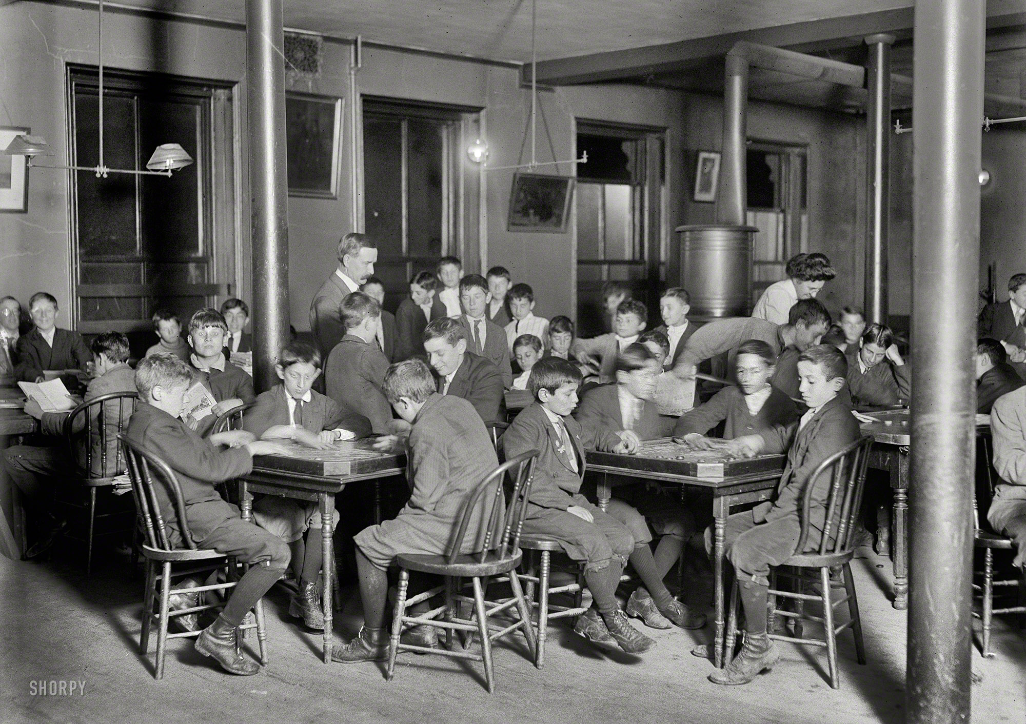October 1909. Boston, Mass. "In the Newsboys Reading Room. Boys seated at tables playing games." Photograph by Lewis Wickes Hine. View full size.