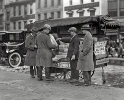 Washington, D.C. "Newsstand, 1925." Out-of-Town Papers, with Information Cheerfully Given. National Photo Company glass negative. View full size.
400 Block of 11th Street NWThis is the same location as another shot featured on Shorpy from a much warmer season in 1921 https://www.shorpy.com/node/11170.
Bandage on fingerLikely a "paper" cut.
The HeadlineIn 1925, the S-boat class of U.S. Navy undersea vessels suffered a series of accidents.  Among those was an episode on January 29, 1925, involving submarine S-48, that matches the Chicago newspaper's headline.  Traveling up the New England coast from New London, the vessel encountered a fierce winter storm with strong gales which initially hurled the ship up on the rocks of Jaffray Point near the entrance to the Portsmouth, N.H. harbor.  Not only did the gale force the sub up onto rocks, but the landing caused a chlorine leak on board that forced the crew to huddle in one end of the ship.  Fortunately, a later gale and its wave refloated the sub, and pushed it into the relative safety of the harbor, where the crew could be rescued. Meanwhile, the same storm caused blizzards further down the east coast, which may account for the snow and slush in the gutter.    
(The Gallery, D.C.)