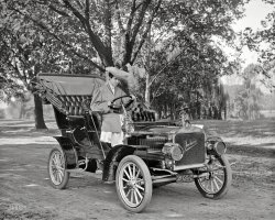 Washington, D.C., or vicinity circa 1908. "Mrs. John E. Harris." At the wheel of a shiny new Jackson. Harris &amp; Ewing Collection glass negative. View full size.
Well not *too* shinyA fair bit of mud on the inside of the fender, though I suppose it was unavoidable given the roads of the time.  By the way, I suspect that Mrs. Harris wasn't actually driving the car, but just posing for the photographer.  None of her clothes are being buffeted by the wind and her posture seems rather contrived.
I thought she looked familiar....
Patched Tire?Maybe not so new considering the condition of the tires. Great pic though.
Count &#039;emEach tire/wheel has four "stems" projecting inward. One looks like a standard stem for filling the tire with air. The other three are different from the first, but they look alike. Any idea what they were used for? 
[They're rim clamps. -Dave]
Re: Count &#039;emThere are five "stem-like" projections on each wheel. One of them (e.g., the one at about 1:00 on the right front wheel) is the air valve stem. The four that are spaced at 90 degrees around the wheel are "staybolts" (or "lugs") that held the tire in the rim. A couple of years after this picture, Firestone introduced the "detachable rim" that obsoleted the staybolt system.
Searching for "tire staybolt" should find a Google book with some illustrations that sort of show how they worked.
Jackson and the Indianapolis 300The Jackson Car was made in Jackson, Michigan from 1903 - 1923.  This appears to be a circa 1908 Model C with a handmade leather Maryland license plate.
The next year a standard Jackson car was leading the 300 mile long Wheeler-Schebler Trophy Race at the Indianapolis Motor Speedway (not yet paved with brick) by more than 10 miles when the race was called off because of poor track conditions and a deadly crash.  
No winner of the race was declared, but Jackson announced their win in at least one ad and showed a picture of the trophy in the ad.  They had covered 235 miles (94 laps).
Since Jackson was not declared the winner they sued for the trophy, but the company lost in court.  It was not until many years later they they were acknowledged as the winner of the race.
Only six cars out of 19 were still running when the race was called.  One of those six drivers was Roy Harroun who would later go on to win the first Indianapolis 500 in 1911.  He was also the first person to be presented the Warner-Schebler trophy when he won a 200 mile race at the Speedway the next year.
The 7 foot tall trophy was made by Tiffany and valued at $8,000 by its donors.  The trophy was only the property of the winning company/driver for a year.  When Harry Hartz won the trophy three years in a row, per the deed of gift for trophy, it was permanently awarded to him. He donated it to the Indianapolis Motor Speedway Museum when it opened in 1956.  It is still on exhibit there today.    
A circa 1908 Jackson can be seen in the movie Long Day's Journey Into Night (1962).
(The Gallery, Cars, Trucks, Buses, Harris + Ewing)