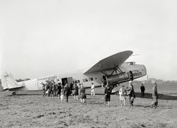 Sept. 29, 1929. Washington, D.C. "Fokker F-32 transport plane at Bolling Field." Note unusual back-to-back engine arrangement (and mechanic stationed aft to keep people from being pureed). National Photo glass negative. View full size.
Bolling Field Everything you wanted to know about Bolling Field:
http://www.airfields-freeman.com/DC/Airfields_DC.htm
Also note the building across the river is very near what is now Nationals Park and part of the Navy Yard .
StreamlinedHow about that aerodynamic windshield?!  Good thing speed and fuel consumption weren't an issue then.
124MThis aircraft was the first of the type built, constructor number  1201. It was also the first to crash, on 27 Nov 1929, just  two months after this photo was taken.  It crashed at Roosevelt Field while demonstrating a 3-engine takeoff. The second engine on the same side failed making it uncontrollable. There were only two injuries, no fatalities, but the craft was destroyed in the ensuing fire. This photo was taken only 16 days after the plane's first flight.
Not the only design bugApart from the poor cooling on the rear engines, their props would also loose efficiency as they would turn in the wake of the forward prop and of all those struts. They would be quite noisy, too, for the same reason. 
And propellers turning undernath a wing (rather than in front of one) also tend to decrease overall lift, especially at low speed. Not to mention that they skew the spanwise lift distribution, which would increase drag again. 
But every design is a compromise. The designers had good reasons for what they did.
- They needed four engines for their power and for redundancy.
- Installing the 2 by 2 reduced adverse yaw if one engine failed.
- The nacelles could be suspended close to the struts.
- The engines were better accessible for maintenance.
- A high wing gets the fuselage closer to the ground overall - a boon when airport facilities consist only of a stool or pedestal.
- And so on.
Look how close they get to the turning(!) prop. Eeeek!!! That's asking for trouble (of the spattering sort), even with the watchdog in the white overall. 
The Boeing 747 of its dayAlthough only ten were built and just two made it into scheduled service, the Fokker F-32 was the era’s largest successful passenger plane, with seats for 32 (including two under the cockpit). For 1930 it was quite advanced with two-way radio and two toilets. The push-me pull-me engine design (as such configurations were called later) was chosen to reduce drag from four engine nacelles to two. The rear engines however, as was mentioned, did not cool adequately and their propellers’ efficiency was affected seriously by the two up front. I said "successful" because in 1929 the Germans rolled out the massive, 12-engined Dornier DO-X, with the same push-me pull-me arrangement. Too many problems, however, kept it from the market.
Universal Air LinesStill lives on, in a manner of speaking, as a predecessor of American Airlines.
A four engine aircraftbuilt in Teterboro N.J. by Fokker America, not very successful from the engine placement, the rear engine could not be cooled properly, 10 were built, they cost $110,000 in 1929.
Standard Fokker ConstructionNeat tandem rudder.  You can see the cables for the rear control surfaces piercing the fuselage just behind the 'Universal Air Lines System' logo.



The Baltimore Sun, September 22, 1929.

Largest U.S. Land Plane Is Tested


Thirty-Passenger Fokker One of the Five Ordered For Transcontinental Air Service.


The largest commercial airplane ever built in American and the largest land plane in the world was tested publicly last week, with results highly gratifying to its designer, Anthony H.G. Fokker.

This huge plane is the first of a group of five ordered by the Universal Aviation Corporation for use in its transcontinental services. It has accommodations for thirty passengers in day flights and for night flying can be converted into an aerial Pullman with berths for sixteen. Adequate facilities for the comfort of passengers in the way of lavatories, serving pantries and the like have been provided.

From tip to tip of the wind the span is 99 feet, giving a wing area of 1,350 square feet. Its length is 69 feet 10 inches and its height is 16&frac12; feet. The weight empty is 13,800 pounds; fully loaded, 22,500 pounds. The power plant consists of four air-cooled engines, each developing 525 horse power. The engines are arranged in tandem, fore and aft on each side of the cabin. For day flying the plane carries 400 gallons of fuel and 40 gallons of oil, giving it a range of 480 miles. As a night plane, the fuel capacity is 700 gallons, with the increased range to 850 miles. The crew consists of two pilots, a radio operator, one day steward and two night stewards. &hellip; 

In its general form of construction this plane, called the F-32, follows the standard Fokker methods. It has an all-wood veneer covered wing of the cantilever type, and all other structural parts of steel tubing.

Windshields plus French FarmansThe forward-slanted windshield was fashionable for passenger aircraft in this era. The slanted winshield helped solve the problem of lighted control panel instruments reflecting off the normally backward-sloping windshield at night, but it turned out that the forward-sloping windshield would reflect ground lights instead, especially during landings. Eventually the drag factor and the introduction of tinted plexigas in the 1930s put paid to this idea of forward sloping windshields. 
As for the odd four-engine arrangement, the French were still using it with their massive Farman 220 series of airliners and bombers in the 1930s. One of them, the converted airliner "Jules Verne", was the first Allied bomber to bomb Berlin in 1940!
When planes had mudflapsThose were the days!  Seriously, though, some people thought it worth walking across a muddy field and through a prop wash (must have been fun in cold weather or rain), then putting up with what must have been an incredible vibration and din and a roller coaster ride for several hours.
Big Boy!Here’s a look at how massive the F-32 was.   In 1931, an earlier Fokker model, an F-10 Trimotor, crashed near Kansas City, Kansas, killing all eight people on board including Notre Dame football coach Knute Rockne.
One lucky Fokker...was the centerpiece of a Los Angeles filling station through the '30s. The F-32 was purchased from Western Air Express and painted in Mobilgas colors. Fuel islands were put under the broad wings. The ship lit up at night, and the gas monkeys could fire up the forward engines, to the delight of customers.
Bob's Air Mail Service Station
Tony Fokker's personal F-32, which he'd had kitted out as a plush flying home and office, wasn't so lucky. His business and the country's went to hell at about the same time, and he had to sell the plane. The fuselage ended up in West Virginia as a house trailer, and in the great Ohio Valley floods of 1937, even that was swept away.
It's anybody's guess how long Bob's Air Mail plane could have lasted in the elements. The F-32s were all wood except for their chrome-moly fuselage framing. (edit: The plane was scrapped in 1939.) 
(The Gallery, Aviation, D.C., Natl Photo)