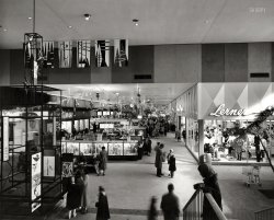 1958. "Harundale Mall, Glen Burnie, Maryland. Interior view." The first enclosed shopping center on the East Coast. Nirenstein Collection print. View full size.
Harundale 1947The construction of the houses in Harundale was the subject of an article in Popular Science in November 1947:    
The factory for constructing the houses was located on the site of the future Harundale Mall.
Nearly all the little houses constructed per the above article are still standing.
Now Harundale PlazaThis is a mile away from my house. The site is now a strip mall with a Burlington Coat Factory, some crap stores, empty storefronts, and an Outback. Not a prime location. Hasn't been for decades. Though I do remember it still being somewhat viable in the 80s, as my school chorus traveled there to sing at Christmas one year.
Delightful versus frightfulI don't believe Mr. Loewy had his elegant hand in this particular project.  We have recently seen good examples of 50's style done right, put in perspective by this more typical sample.  
But I suspect there are few complaints about the decor on this cold December day, when the weather outside is frightful, but the fire is so delightful.
Harundale MallThis is the first mall I ever went to. It was on Ritchie Highway, a full access road that connected Annapolis to Baltimore. It was a huge thrill. I remember spending a whole day there with my mother Christmas shopping. They played Christmas music all through the mall, and they must have played "The Christmas Song" by the Chipmunks a thousand times. We ate lunch at Read's Drugstore (you can see it down on the left). On the way home, we ate dinner at the White Coffee Pot. Several years later, a huge Two Guys discount store and an EJ Korvette store opened nearby.
An early mall with kiosksIt's interesting to see an early mall like this with lots of interior kiosks housing smaller stores -- while these are quite common in modern malls, in the other early malls you've shown on the site (like Southdale), as well as the malls I grew up with in the 1970s, these were rare -- the central hallways were pretty open except for the occasional fountain and the like.
(The Gallery, Stores & Markets)