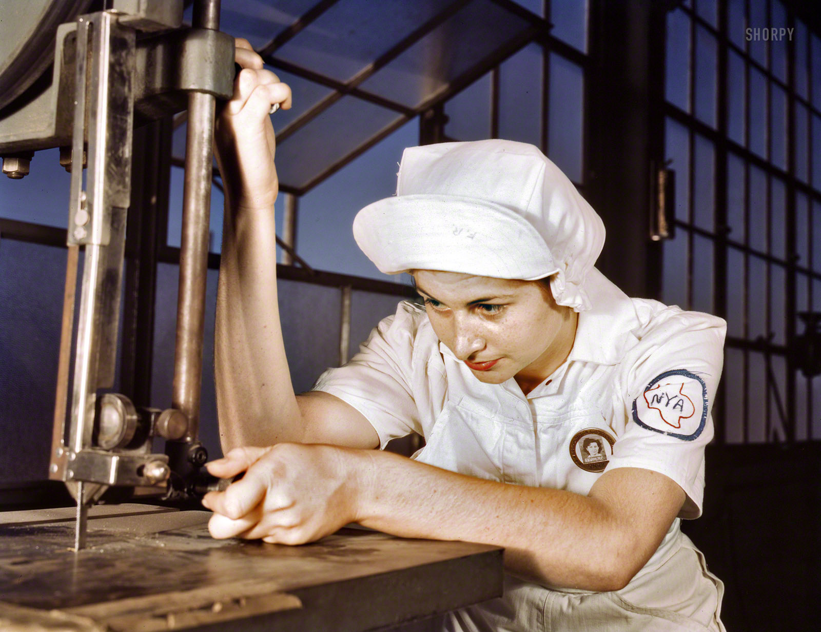 August 1942. "Women in white doctor Navy planes (motors) at the Naval Air Base, Corpus Christi, Texas. Mildred Webb, an National Youth Administration trainee at the base, is learning to operate a cutting machine in the Assembly and Repair Department. After about eight weeks as an apprentice she will be eligible for a civil service job in the capacity for which she has been trained." 4x5 Kodachrome transparency by Howard Hollem, Office of War Information. View full size.