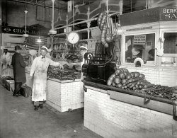 Washington, D.C., circa 1924. "Stephen Frank -- Auth Provision Co., Center Market." National Photo Company Collection glass negative. View full size.
Razed in 1931The block that Center Market occupied is now the home of the National Archives. D.C. still has markets like this. There is the more upscale Eastern Market, the oldest continuously operated fresh food market in the country.
When Center Market was torn down, it was to make way for something more "modern" -- the self-service supermarket, where all the the individuals vendors in stalls were replaced by "departments" under one brand name roof. The 1930s saw an explosion of the chain grocery system, and Center Market was simply too old-fashioned. Too bad the owners had no idea that 50 years later, that antique system would be a tourist attraction.
Still Around!Looks to be some tasty slabs of bacon he has his arm on.  Possibly head cheese, salamis, and kolbas too.
Thankfully, these types of markets still exist.
Cleveland has one that closely resembles this photo. With many and varied vendors under one roof, each with their fresh specialty.  It beats any supermarket, hands down.
http://www.westsidemarket.org/
Detroit has its Eastern Market.  It's not under one roof -- it much too large.  It's an enjoyable adventure on a Saturday morning.  
http://www.detroiteasternmarket.com/
Any others out there?
Despite the cleanlinesslet us hope the temperature in there is a blistering 20 below.
Agree on the BaconSo when did they start producing the fat slabs they now call American bacon? Look at the bacon sold online at those ethnic grocers. Really like these old "market &amp; store" type photos.
O StreetEastern market in DC still has this feel.  Of course, the bacon slabs are in coolers behind glass now.
I am not sure this photo was taken at Center Market.  The "O" Street address in background suggests that it was actually taken at the Norrhern Market, which was also called the O Street market. 
[Look again. The sign says "Branch of" the main store at 620 O Street. - Dave]
Harry Potter and the Half-Baked Hollywood HamNotice the young man to the right of the hanging scales.  Is this a young photo of George Burns, before he took up his alter ego as Harry Potter?
Cleanlinessdoes not seem part of his remit, given the state of his apron.
Center MarketThe wonderful, cahotic chaotic Center Market was located on Pennsylvania Avenue where the Natioanl National Archives is now. A breif brief histroy history of it can be found here.
I&#039;ll take 18 pounds of old Leather Handbags please.
Bacon and BraunschweigerThe sign fragments in the photo are Berkshire Sausage and Charles B. Althoff, 620 O St. N.W., dealer of bread, pies and cakes.  The faded sign is N. Auth Prov'n Co., Wholesale &amp; Retail.  Smaller signage includes Positively No Checks Cashed and These Stands Close Sat. at 6 P.M. During June, July &amp; Aug.



Washington Post, October 19, 1924

Ask For Auth's Always!


Steaming hot, crisp, tender, nutritious &mdash; just as good to your stomach as it is to your tongue. No wonder thousands of well-fed families start the day with Auth's Sausage Meat regularly.

Auth's Pure Pork Sausage Meat with hot cakes &mdash; is the ideal cold weather combination. Nourishing for breakfast. Satisfying at night. And popular with every appetite all winter long. Think how easy it is to prepare, too. In less than fifteen minutes, you can have a real meal.

Auth's Sausage Meat


Other Auth Products: Frankfurters, Pork Sausage, Scrapple, Smoked Ham, Bacon, Pure Lark, Pork Pudding, Cooked Ham, Royal Pork, Braunschweiger.

(The Gallery, D.C., Natl Photo, Stores & Markets)