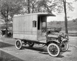 Washington, D.C., 1922. "J.C.L. Ritter -- Polli Food Products truck." National Photo Company Collection glass negative. View full size.
What kind of headlights are those?Check out the car right behind the Model T.  What kind of headlights are those?  Looks like a modern LED lens.  Could this be some kind of gas fired light? 
[You're seeing the pattern of the headlight lens. - tterrace]
Vehicle ID&#039;sL to R:Apperson Jackrabbit(note animal on radfiator core),Ford model TT (ton truck), Packard, unknown dump truck
Lamp Covers?It's possible that those are protective lamp covers. Lots more rocks in the road and hard to find parts (no standardization of lamps yet, so probably needed to order to replace) created such a need.
Of course, in many jurisdictions these days, covers over headlights aren't legal, although you still see them, but in some sort of plastic.
More universally required these days are fenders and/or mudflaps, neither of which is on the Model T truck's rear wheels. 
Classic trucksI really like these old-fashioned cars and trucks. Hard to ride on, difficult to drive, but sturdy and resistent. Those wooden bodies lend them a certain look and feel I find really attractive. And they were very recyclable - once you wrecked the truck, you could use the remains of the body in the chimney. 
Yes, LensesYes, those are glass lenses on the Packard. Possibly from the Warner Lens Co. Here is a similar set on a Stutz.
Heavy Load - UnloadedThis woody must have been for lightweight goods transport - eggs, bread, etc., since the weight of all that wood is a major load all by itself. Love the trim over the side window.
Nothing personalCould these vehicles be destroyed by termites?  (No offense to tterrace).
Plywood?Seems they took advantage of a relatively new product,  the plywood industry was born around 1905-7 in Oregon although the Egyptians and Chinese had forms of it 3500 years back.
Note the TiresThe Ford is equipped with non-skid tires. If you don't believe me, you can read it for yourself: The words "NON-SKID" make up the siping (tread pattern).
Carpentry and axleCarpentry and axle grease...Rapture!
Ford Truck ChassisFord supplied the bare chassis, the dealer or the buyer supplied the body.
Warner LensHere is a closeup of the Warner headlamp lens introduced in 1912. Production stopped sometime in the late teens. There is an ad for the lenses here: http://the-master-craftsman.blogspot.com/2010/12/patented-in-1912-two-wa... 
(The Gallery, Cars, Trucks, Buses, D.C., Natl Photo)