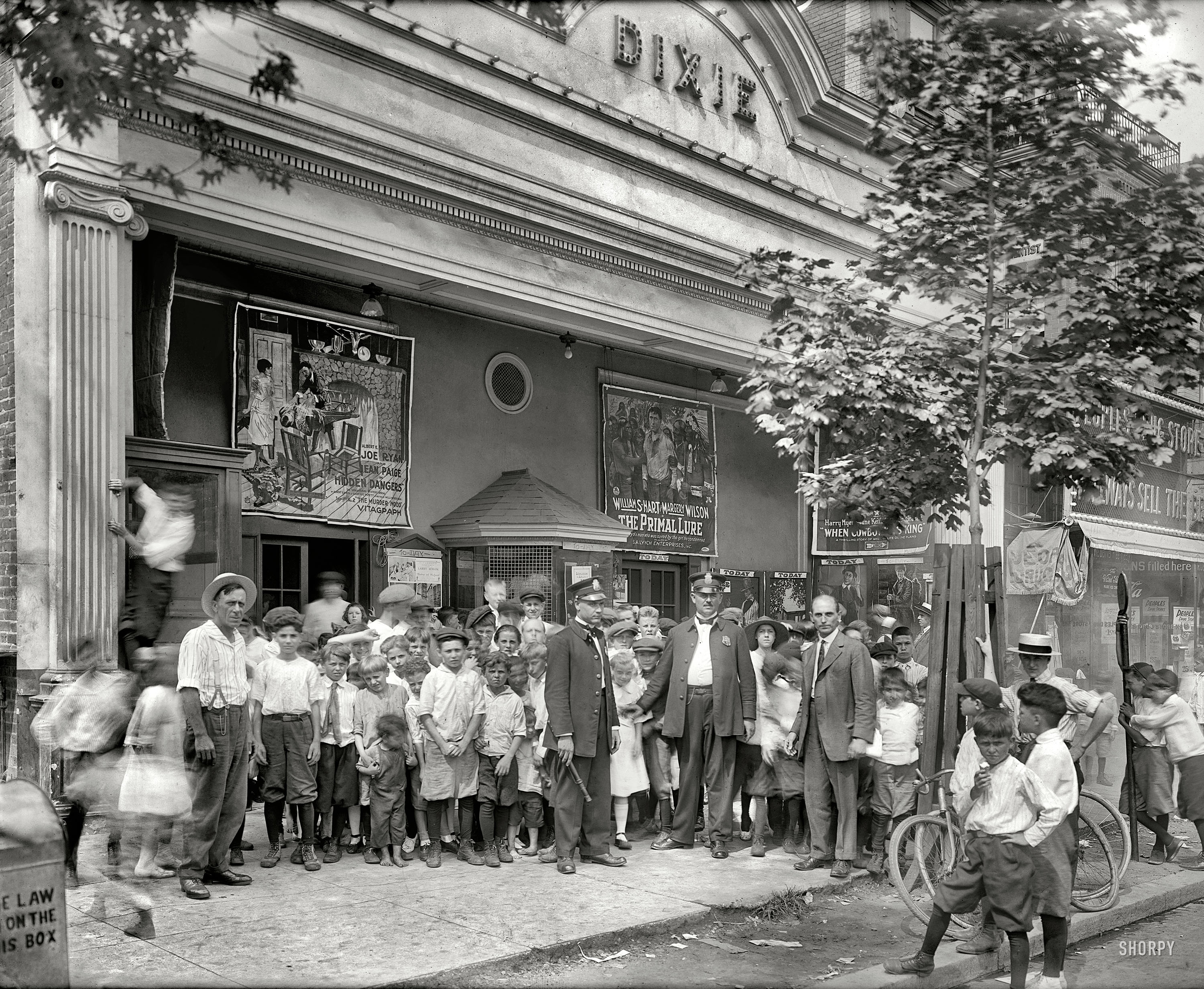 Washington, D.C., 1920. "Dixie Theater crowd, H Street." Now playing: "Hidden Dangers" (Episode 2, "The Murder Mood"), "The Primal Lure" and "When Cowboy Was King." Kids get in for 11 cents! Next door: People's Drug Store No. 5. National Photo Company Collection glass negative. View full size.