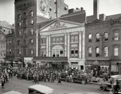 Washington, D.C., circa 1920. "Crowds at Metropolitan Theatre, F Street N.W." National Photo Company Collection glass negative. View full size.
Lotta LookingI see Lotta Miles, the Kelly Springfield Tires lady, looking over the scene.
Block is much the same todayFrom what I can see on Google maps, the theater is the only building that is gone on that block The other buildings look pretty much the same today as they did then.
View Larger Map
Personal appearanceMildred Harris Chaplin, the star of "The Woman in His House," made a personal appearance at the Metropolitan, which probably explains the crowd.
Atlantic BuildingThe Atlantic Building, to the left of the theater, was a hotbed of music and art in the 1980s. "The Bootery Footwear" housed a carryout which featured the "bone fish sandwich," a big piece of fried fish, complete with bones, on a bun.
Superproduction Premier


Washington Post, October 10, 1920.

At the Picture Houses.
Metropolitan &mdash; "The Woman in His House."


An event of particular importance in the picture world will be the first showing on any screen of Louis B. Mayer's superproduction, "The Woman in His House," at Crandall's Metropolitan for the entire week. An all-star cast headed by Mildred Harris Chaplin appears in the picture which is said to surpass the "Miracle Man" in heart appeal and has already been booked into a production house in Broadway where it will be shown at $2 prices.

Lotta TalentThe young lady in the Kelly-Springfield ad is Miss Norma Shearer.
It is ironic that the theater is showing a Louis B. Mayer film. In a few years Miss Shearer would become one of the superstars of MGM pictures. She would also marry Mayer's nephew Irving Thalberg. 
An article about the theatreAn article on the theatre:
http://cinematreasures.org/theaters/7629
Not REALLY Still ThereFor better or for worse, these buildings remain as facades only.  A clever compromise has been reached in DC that allows developers to construct modern office space that incorporates the facades of legacy structures such as these. 
No minced words for Mr. MintzIn the 1922 guide book “Historical Self-Guide of Washington The Heart of the Nation. Arlington and Mt. Vernon. A Liberal Education for the Sight-seer" its ads included “‘Mintz the Trunk Man, agent for Indestructo Custom Made Trunks’, who mixed low commerce with patriotic reverence and promised ‘IMMEDIATE repairs to your trunk or leather bag’ located ‘just around the corner from Ford’s Theatre where President Lincoln was shot’”.
Along with trunks and suitcases he offered traveling  bags "for  the  missionary, and leather  novelties". Probably better not to question the juxtaposition of missionary and leather novelties. 
930 F St NWHunh.  930 F St NW, next door to the theater, was the old home of the 930 Club, a well-known alternative-music venue where I saw many a band back in the 1980s.  I think Nirvana was the last band I saw there, with Loop opening up.  If you can imagine Nirvana in that tiny front room; yeah.  It's no mystery where my hearing went.
(The Gallery, D.C., Movies, Natl Photo)