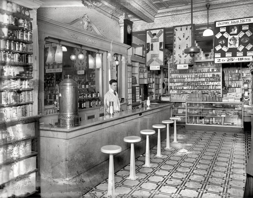Washington, D.C., circa 1920. "People's Drug Store, 14th &amp; U Streets, interior."
Is flyaway hair holding you back? Keeping you home those evenings your friends are out having a gay night on the town? Those loose strands may be a symptom of deeper ills -- malnutrition the consequence of egg-based-beverage deficiency, perhaps aggravated by tooth-brushing with an inferior dentifrice. Ladies, am I talking to you? Then come see this man. He is the gatekeeper to hair-nets, toothpaste, Egg Drinks -- and so much more. (Rubber gloves, for one thing, but that's another story.) The day you pick up a Glemby Hair Net -- or two, or hell, why not a dozen -- is the first day of the rest of your life! View full size.
