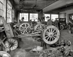 1923. "R.L. Taylor Motor Co." The service garage of this Washington, D.C., Ford dealer, seen earlier here. Here we are 20 years into the Motor Age yet this still has the look of your local Conestoga wagon repair shop. View full size.
Where the term &quot;Grease Monkey&quot; originated.That place is filthy!
What a dump!I don't know how they know where or what anything is in that mess!  Someone could trip over the extension sticking out of the tool box, but he wouldn't fall too far before he'd hit something else! OSHA would have a field day what with all the exposed pulleys and drive belts!
How to Start a Model T
Tractor! Can anyone identify the model of tractor the gents are working on? They have the cylinder head and manifolds off. A ring job perhaps? 
T MEN G MENThere is so much going on in this photo it's hard to start. Out of the three men in the back the one in the suit looks like central casting for a typical G man. The other two staring the camera down look like the are about to teach the photographer a lesson he won't forget. 
It looks like the 2 partial cars in the foreground were early dirt racers the tires on the middle car seem to be caked in mud. All in all it is a fascinating photo and I am sure as I stare at it much more will be revealed.
Tractor:The tractor is a Fordson Model F, manufactured between 1918 and 1928. I agree that they're probably doing a ring job on it; the copper head gasket is lying on the ground, but I don't see the Fordson's head or manifold anywhere. They've removed the steering wheel and fuel tank to gain access to the head bolts. 
There is a complete Model T automobile engine and transmission visible behind the tractor's rear wheels.
Notice the Model T rear differential leaning against the wall in the lower left-hand corner: The spaces in between the wooden spokes have been filled with concrete to provide extra weight -- but why?
Great line shafting on the ceiling, and overall just a great photo from 90 years ago!
Tractor!It's a dismantled Fordson.
Baby It&#039;s Cold InsideHeavy jackets, collars high, window open for some ventilation.  Miserably cold on the hands, especially when you wash a greasy part with gasoline.
14th and TIt seems the building, at T and 14th Streets NW, lives on.
Red meat for gearheadsNeat little slice of life here, this is the era when Henry Ford was trying to make the same splash in the tractor market that he had in cars, even metropolitan dealers were getting shipped unordered tractors they were expected to find customers for.
Concreted wheels were one of the tricks used on "Doodlebug" home-made tractors to eke out a bit more traction, somebody had a side project.
[That's clay, not concrete. - Dave]
I'm fascinated with the floor fixture they have an entire Model T rear axle, torque tube, dogbones, and all, mounted on, lifts as we know them were a few years down the road and this looks like a well thought out method of doing major work without lying on your back for hours.
(The Gallery, Cars, Trucks, Buses, D.C., Natl Photo)