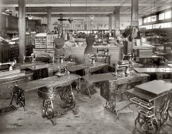 Washington, D.C., circa 1919. "Oppenheimer's dress shop." Haunted by a few spectral customers. National Photo Company glass negative. View full size.
Old Sew and SewsI'm betting these machines were on their way out to make way for the latest electrically powered models.
Hello, Ghost?All of the machines appear to be approximately the same with slight variations in their support tables. Some have one style drawer handle, others have a different one. But the machine at the front left is of an entirely different era or manufacturer. I wonder if that is a used machine somebody traded in when they bought a new Singer.
There is also a telephone sitting on top of all the cabinets on the far left. I am guessing that is a guest phone for the ghosts because I can't imagine anyone else being up there to answer it.
InsightGreat photograph.  It's neat to see all of the original displays, forms and sewing machines.  Ironically, I love taking the iron bases and making new tables out of them.  Oh, to have all of those models in hand!  Thanks for posting this.
No cash registersIn the background we can see the pulleys and cables that were part of a cash handling system long gone from our midst.  The clerks would write up the sale, and send the ticket with the cash in a little wooden barrel, zipping along the cables, to the clerk's office (I think that's it at the left, note the candlestick telephone up near the ceiling).  The little canister or barrel would get sent back to the clerk with the Paid receipt and any change in it.  As a kid in Upstate NY, I'd be entranced by watching this system in operation at a local dry goods store.   Part of this system is still in place as a piece of historic technology, but the rest was supposedly packed off to the Smithsonian some years ago.      
CabinetsIn 1868, the New York based Singer Brothers Company decided to locate the Singer Cabinet Works in South Bend, Indiana (my hometown). The area contained a rich supply of fine walnut and oak lumber with which Singer would build cabinets for their sewing machines. By 1907, 10,000 cabinets a day were produced in South Bend, and by 1914 the company had gained 75% of the world’s market of sewing machine cabinets. The company remained in South Bend until 1955. Lewis Hine (no surprise) took some photos of child laborers outside the plant in the early part of the century.
Hooterville Telephone CompanyLooks like Oliver Wendell Douglas isn't the only one that had to climb before making a call. Between pedaling the machines and ascending to the phone, I imagine the shopkeeper kept rather fit.
Willcox and Gibbs The little machine in the left foreground is a Willcox and Gibbs chain stitch machine which was a major competitor of the Singer Co.
 It was manufactured with very little change from the middle 1860's to sometime in the 1960's I think.
 Electrification of most of the older machines was available
a moderate cost and became popular as electrical power reached the rural areas.
 Nice picture!
The Old Man and the SpoolOn the shorter cabinet behind the dress dummy on the left can be seen “M. Heminway &amp; Sons Co.”  General Merrit Heminway was the first person to wind silk on a spool in the U.S. and, in 1849, began the manufacture of “sewing silks of all kinds” according to the Web site History of Litchfield County (Connecticut). From the mid-1800s through 1917, his company (formerly Bishop &amp; Heminway) was called M. Heminway &amp; Sons Silk Company.  He was long gone when this photo was taken unless he made it to age 119. To the right we see “Beldings Wash Emb’dy (embroidery but you knew that) Silks” which would have come from Belding, Michigan, called the “Silk City” because of all the silk mills there.  
My mother had a Singer machine very much like those in the photo, most probably used before her by her mom and perhaps her mom’s mom. It had rounded drawers like the one in the foreground. I remember its shiny black finish and gold leaf decoration, and the clever way the machine could be rotated 180 degrees to disappear into the cabinet, with the hinged panel on the left flipped over to create a small desk. Most of the machines here have the same set-up. It just occurred to me that a similar arrangement could be designed for computer monitors. I'd name it "SmartDesk".
(The next day) A revisit to "Little Shop of Singers" and looking at all that sewing machine furniture inspires an alternate title: "Little Shop of Drawers".
IDEAL FAVORITE Sewing MachinesTwo brands which appear to be electric models.
Still In UseMy father rebuilt my grandmother's Singer machine approximately 15 years ago.  On a whim he went to the local sewing shop that was a Singer dealer looking for a replacement leather belt.  To his surprise Singer still supplied the leather belts and a few other parts for these old machines.  The reason was that many were still in use in locations with no electricity and in third world countries. 
Hey!  There&#039;s my Singer!Right smack dab in the middle of the 1919 photo.  Actually it was my grandmother's and handed down to me.  You can't imagine the fun we bunch of urchins had pedaling that thing circa 1969.
Hand cranksThe Favorite and Ideal machines are hand cranked. 
The machine to the right of the center mannequin is Singer Model 31-15 for light industrial use. Many of them are still in use today (usually electrified); they're known as 'the tailor's machine'.
Terrific machineMy mother had a degree in Home Economics and was an expert seamstress. She used to say that the best sewing machine she ever owned was her Singer, which was very similar to the ones shown here. And that included all the computer-driven models she also owned. The Singer was a brilliantly created machine - very responsive and easy to use. Some basic designs cannot be improved upon. Well, okay, maybe a little, but not much.
(The Gallery, D.C., Natl Photo, Stores & Markets)