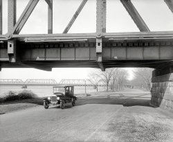 Washington, D.C., circa 1926. "Ford Motor Co." is all the caption says. Who can pinpoint our location using the visual clues provided? Extra credit for Street View links. National Photo Company Collection glass negative. View full size.
Same abutmentsIt looks as if the bridge itself has been replaced over the years, but the stone abutments appear to be original! 
East Potomac Park / Hains Point areaTaken on what is now Ohio Drive under the railway bridge with Long Bridge (over the Potomac) in the background.
Ohio DriveIt's Ohio Drive Southwest with the two bridges next to the Potomac. It appears as though more bridges have been added between them.
View Larger Map
14th Street BridgeLooks like this was taken along the Mount Vernon trail looking south, just under the 395/14th Street Bridge.
[The right bridge, but you're on the wrong side of the river. - Dave]
Arlington HouseLook through the second truss from the left and you can see Arlington House, Robert E. Lee's old house in the middle of Arlington Cemetery.
Horse hitching post?Just to the right of the lamp post in the center of the photo is a smaller post with what looks like a short rope and loop. Is this possibly an equine hitching post, hardly used any more since these four-wheeled things came along?
(The Gallery, Boats & Bridges, Cars, Trucks, Buses, D.C., Natl Photo)