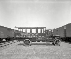 Washington, D.C., circa 1917. "Harry Haas -- Jacobs truck." Prehistoric "transportation," complete with irony quotes. National Photo. View full size.
Ship By Truck!



Washington Post, December 10, 1919.

&#8220;Ship By Truck!&#8221;
It's Quicker.
Long distance out-of-town hauling our speciality.
Phone North 9500, North 9501. 
Jacobs Transfer Co.,
111 Florida Ave.


Everything Old Is New AgainAre those solid rubber tires?  If so, bet it was a rough ride.
All it needs is to get the rims chrome plated and maybe add some "spinners" and it would be "da bomb" today.
Run-FlatsThese must be the original puncture proof tires.
Rim questionFive out of six spokes on the rear wheel have some kind of clamp on them.  Any ideas what it is?
[My guess: They hold the inner and outer halves of the rim together. - Dave]
Tools Could they have made the sign for the toolbox any larger?  WOW!
Rim Clamps For Chains?I believe I have seen these types of clamps on other old vehicles to secure tire chains.  
Re Rim Question and Everything OldThey're some kind of spoke clamp. Yes, those tires are solid rubber. Although pneumatic tires had been available for passenger cars since shortly before the turn of the 20th Century, pneumatic truck tires did not come along until 1919. Solid rubber vehicle tires as on this baby were last made in 1929. By the way, this is a good opportunity to suggest replacing your tires if they're more than six years old, the limit generally given by the industry. (I attended a hearing on a State of Maryland tire aging bill in Annapolis a few months ago.) Your tire "birthday" appears on the sidewall after the letters "DOT" (Dept. of Transportation). You should see four digits; the first two are the week of the year the tire was made, and the second two are the year, so e.g., 3009 = the 30th week of 2009. Even if your low mileage 1998 luxo motor home's original tires look good still, they aren't, despite how much tread they have.  
The Award Winning White TruckThe truck is a circa 1916 White.
Based on similar pictures it is most likely either a 3 or 5 ton model.  In 1918 wheelbases for these big trucks were 163" for the 3 ton and 169" for the 5 ton.  These heavy model White trucks changed very little in outward appearance all the way through about 1928.  
White Trucks were used extensively throughout WWI overseas.  "In the Battle of Verdun the only White trucks to break down were those disabled by shells.  The result was that 2,500 of them [the White Standard Model A] received the distinction of [being awarded] France's Croix de Guerre.'" (Time Magazine, Sep 26, 1932)  I wish I had more information about this story.
Smaller White trucks were the chassis underpinning the buses in Yellowstone Park from 1916 through WWII.  The story of these buses is at the following web site.
http://www.geyserbob.org/Buses-White.html 
(The Gallery, Cars, Trucks, Buses, D.C., Natl Photo, Railroads)