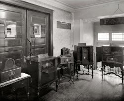 Washington, D.C., circa 1929. "Loomis Radio School." A display of Fada radio sets. National Photo Company Collection glass negative. View full size.
Reply to DbellToo late.  It was 15 yrs. ago and we ended up donating them to a charity's thrift store (who really did not seem too excited to accept them) along with lots of other items I thought would have been snapped up by collectors.  It was before E-Bay.  
Famous caseHere's a bit of trivia about Fada: the 1927 Supreme Court of Canada decision in Fada Radio v Canadian General Electric is frequently cited in Canadian patent law. Fada challenged the validity of CGE's 1920 Canadian patent 196390 on Irving Langmuir's "current amplifying system" - and lost. (The court ruled a false statement to the examiner does not invalidate a patent if there is no fraud.) The patent, as I understand it, was for a 2-stage radio with an RF amplifier/detector first stage and an audio amplifier second stage.
FA.D&#039;A.FADA was an acronym for Frank A. D'Andrea, the radio company's founder and CEO.
Fada Flash-O-GraphThe "flashograph" on the models shown here was a strictly mechanical arrangement of notches in the tuning dial and a switch actuated by the notches which lit a pilot lamp when the corresponding station was tuned in.  It was more of a novelty than a true tuning indicator, as it relied on accurate dial calibration which would slip over time as components aged.
Later on Fada added a true tuning indicator which was activated by the automatic volume control signal of the radio circuit that would both tell the operator when the station was tuned in for maximum signal strength, and the call (name) of the station being tuned by the mechanical dial indicator illuminated by the pilot lamp.
The dials had to be customized for the area where the radio was to be used.
Here's a link to an article that outlines early tuning indicators.  http://ow.ly/dRRBA
Top of the range MaThese must have been the real top of the range radios back then, some models cost $228 which is equal to about $3200 today. Advert from Spokane Daily Chronicle 1930 here. No doubt a Shorpyite will explain just what a flashograph is.
Re: Top of the range MaAnd those prices did not include the tubes!
Unwanted ConsolesWhen my mom passed and we were emptying our her Ct. home of 55 years, we found three beautiful condition full size wooden with bakelite knobs, console radios from the 30's &amp; 40's in her attic.  One was a Crosley, one a G.E., can't remember the third brand, but we put them in the estate sale for $35 each (2 still worked).  After four days of crowds buying her stuff, we still had not had a single offer on any of the radios, so we put "free" on them.  Still no takers. Seems nobody has the space to store them and prefer their pocket size Ipods.  I suppose it's like strapping a full size grandfather clock on your back instead of wearing a wrist watch.   
Re: Unwanted consolesI'll gladly pay for shipping!!!
Those radios were very expensiveSecond from left with an antenna mounted on the side is the Fada model 70 that was available in 1928 and 1929.  According to the Fada dealer price list from December 1, 1928, the Z version of that model cost the dealer $204 and carried a recommended retail price of $340.  Ford's least expensive model A roadster cost only $385 at the time.
1929 Radio CabinetryLike most other radio companies of the day, FADA used beautiful mahogany/walnut veneers &amp; hardwoods to make their cases. Seeing this display makes me recall the scent of the brown paste wax we used on our pre WW2 radio to keep it looking beautiful well into the 1950s. After we got our first TV, the big console radio gradually received less attention.
(Technology, The Gallery, D.C., Natl Photo)